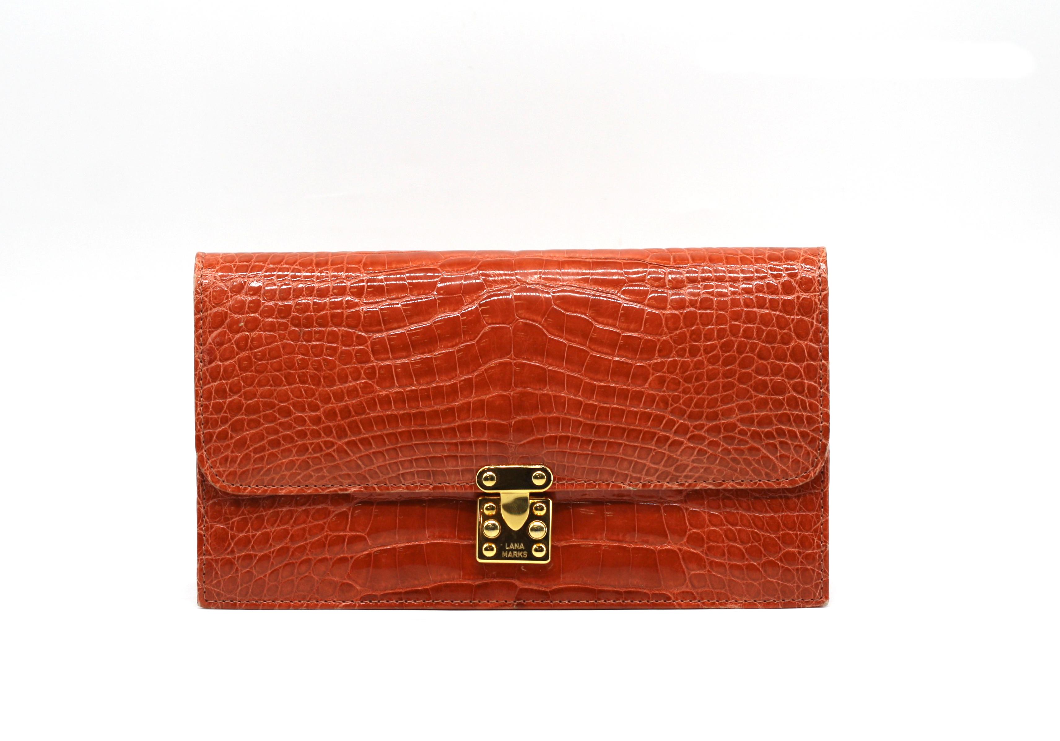 Lana Marks Orange Alligator Clutch
Rectangular with gold-toned hardware, the flap with push-latch closure, the divided cream leather-lined interior with a zipper and a slit pocket. (wear to underside edges)
Height 5 in., Width 9 in., Depth 2.25