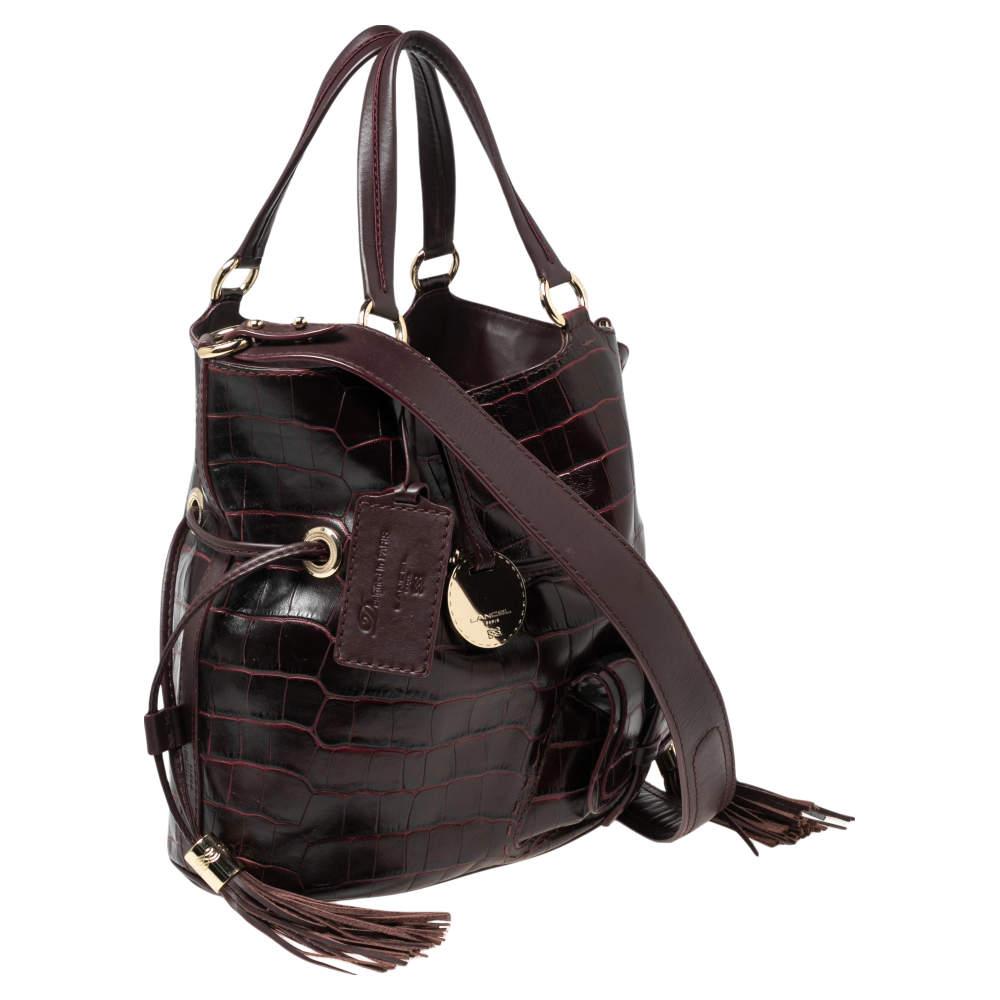 This Premier Flirt bucket bag from the House of Lancel is made to offer practical ease and luxury. It has been created using burgundy croc-embossed leather on the exterior and comes with gold-toned fittings, dual handles, and tassel charms. It comes