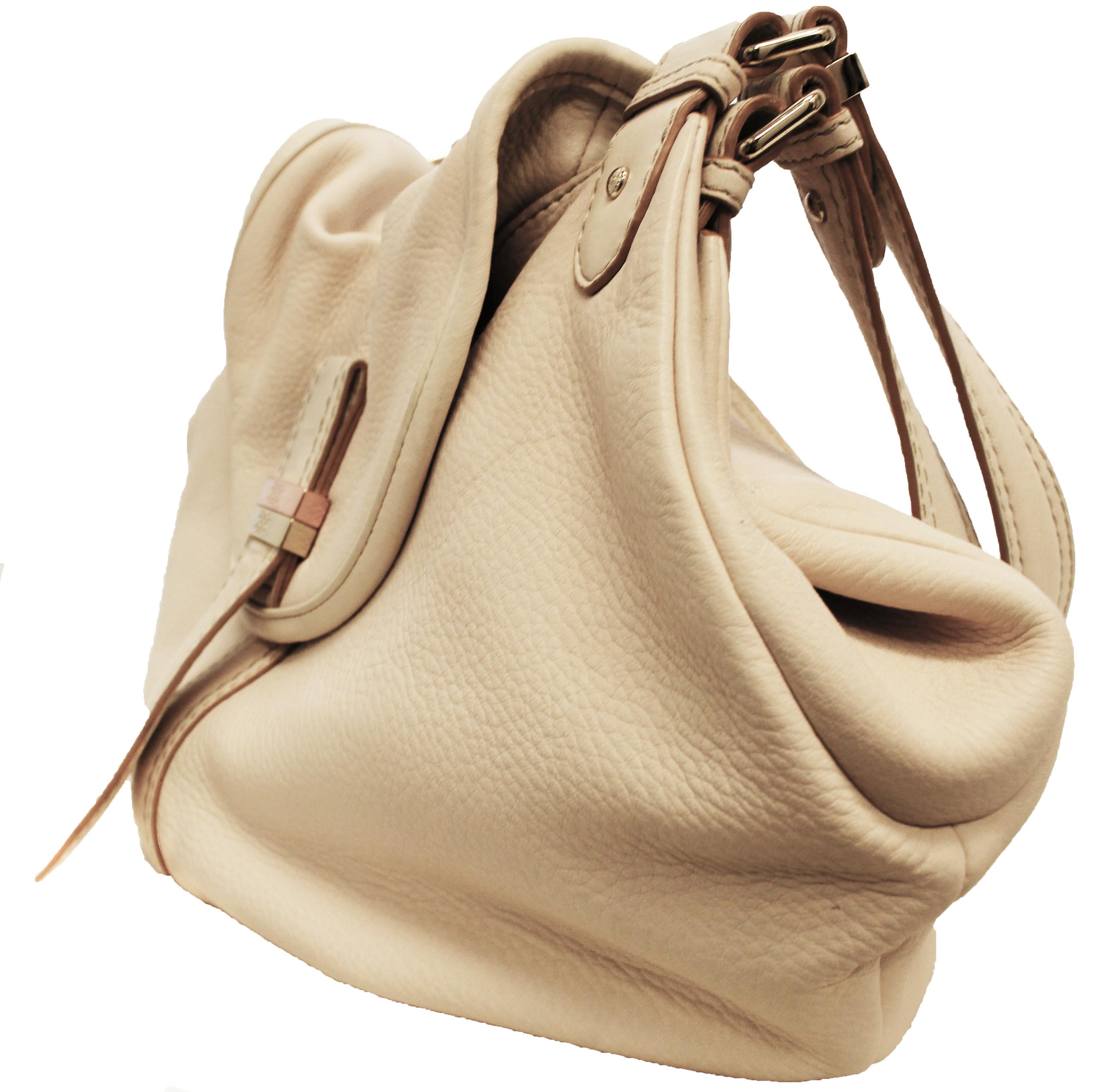Sac à bandoulière à deux anses en cuir de galet ivoire, avec des accessoires en métal doré.  Ce sac possède une grande ouverture centrale doublée d'une magnifique toile verte et rose, ce qui lui confère un look très chic !   Pour la fermeture, un