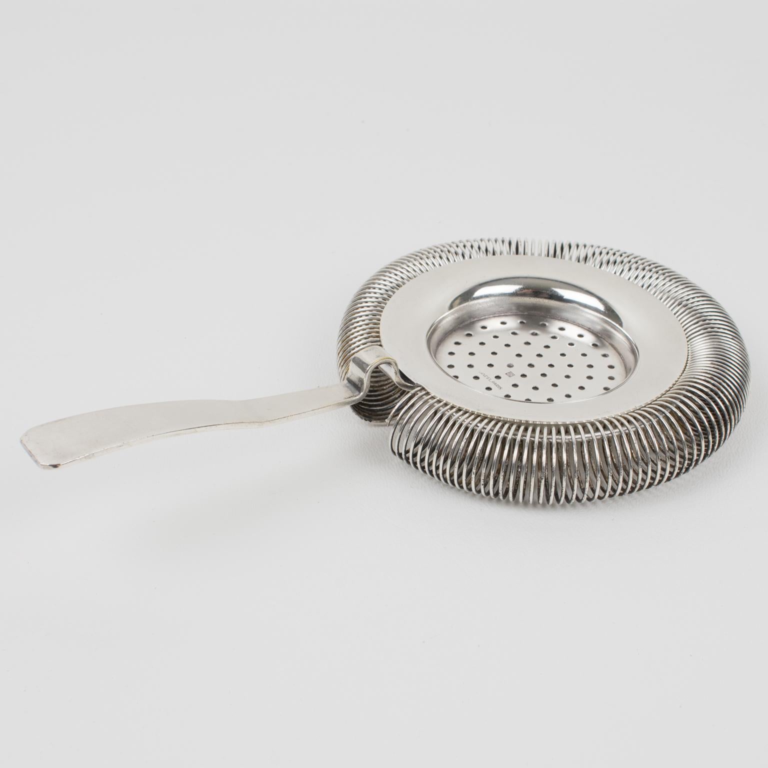 La Maison Lancel, de París, diseñó este colador de cóctel plateado. Utilizado en una coctelera tipo Boston, el filtro colador permite verter sólo el líquido en el vaso, eliminando el hielo. Es el accesorio perfecto para mezclar bebidas y cócteles