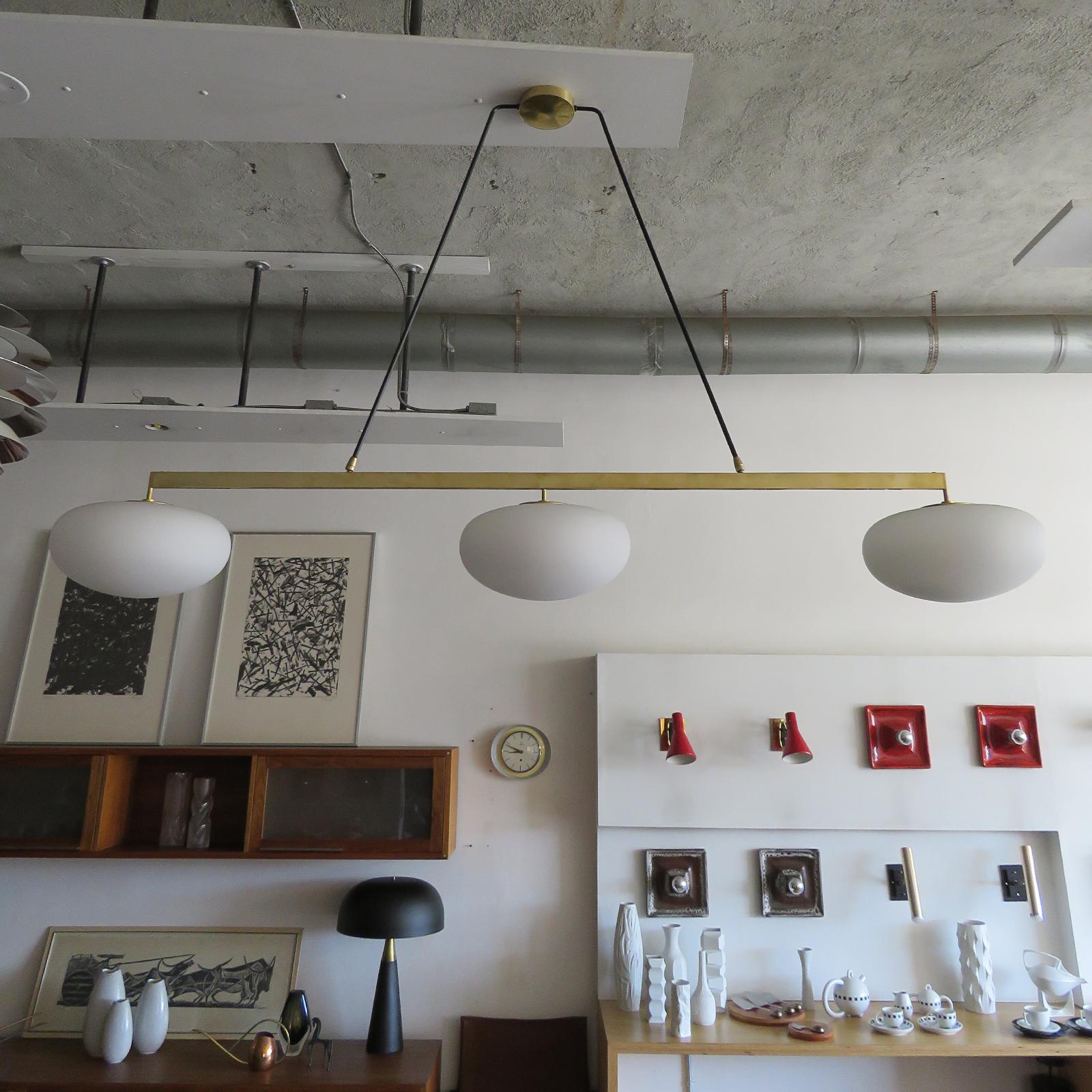 Splendida lampada a sospensione lineare di grandi dimensioni di Gallery L7, realizzata e rifinita a mano a Los Angeles in ottone americano con finitura in ottone invecchiato e tre globi in vetro opalino opaco, misura 72 x 40 x 13 pollici, tre prese
