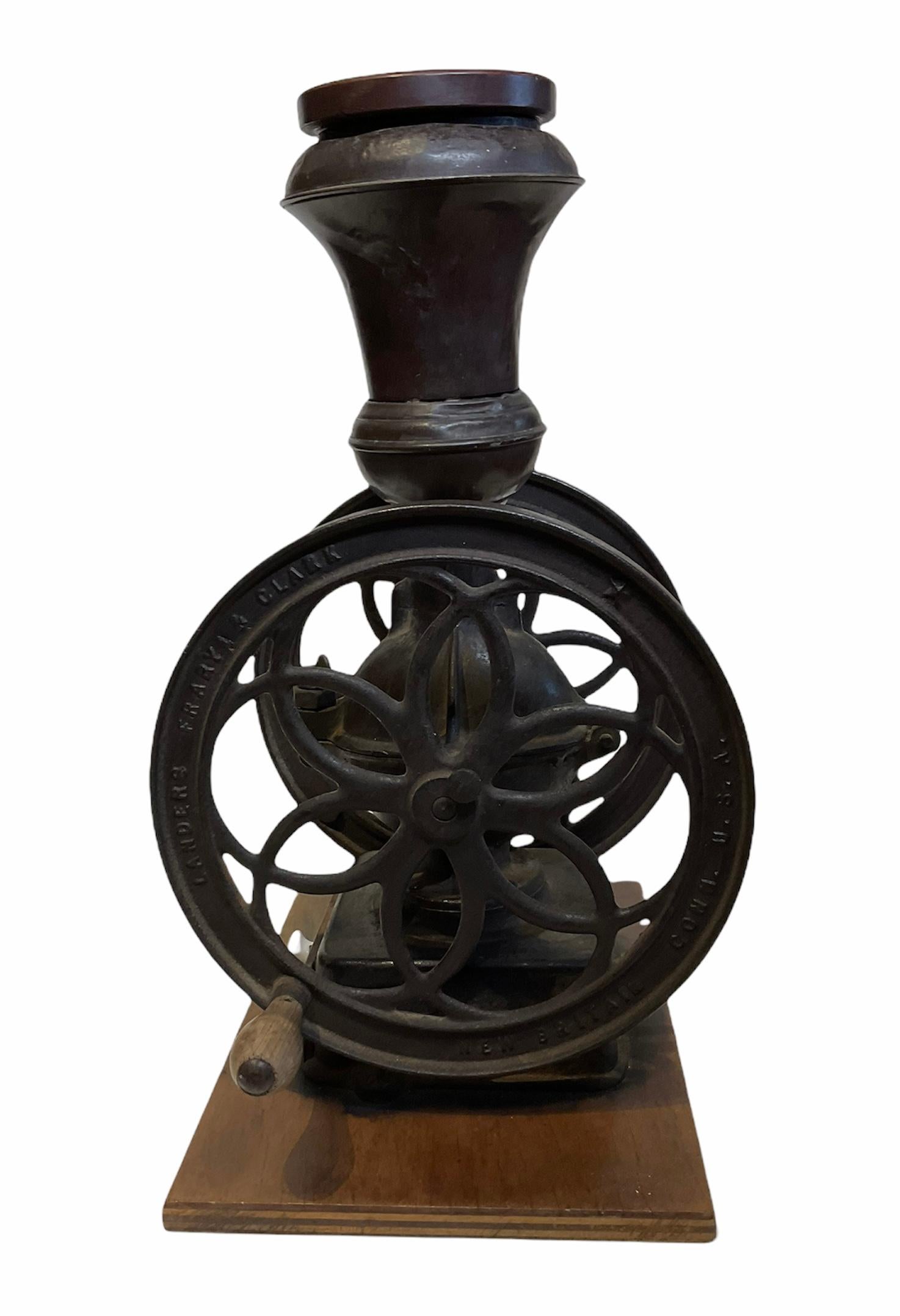 This a large and heavy Landers, Frary & Clark cast iron coffee grinder#20 1/2. It has a bell shaped nickel hopper with a flat wood lid and two flywheels adorned in the center with a six petals pierced flower. Also, they have written in raised