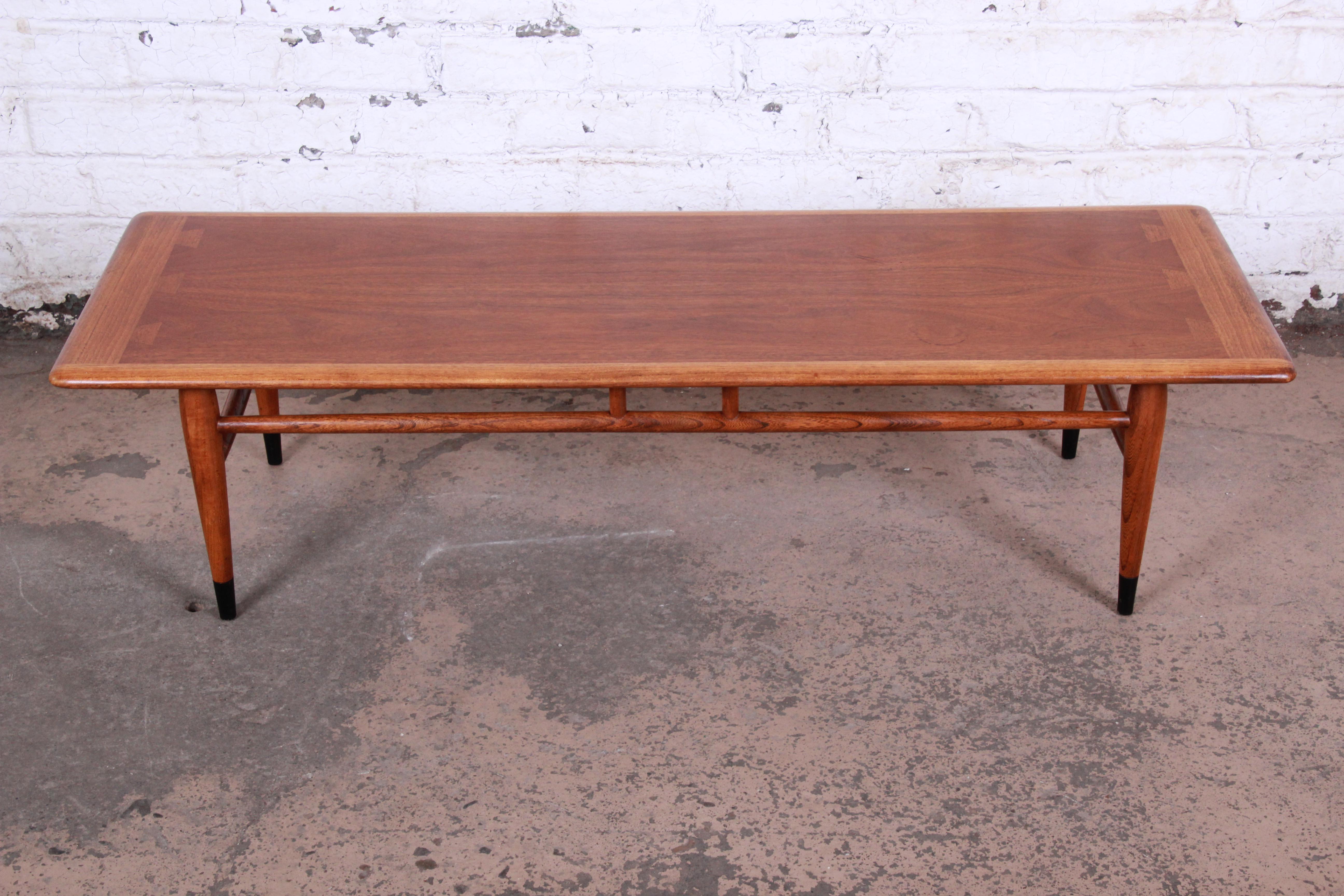 A gorgeous Mid-Century Modern coffee table from the Acclaim line by Lane. The table features beautiful walnut wood grain and unique dovetail joint design. It sits on tapered legs with a sleek stretcher connecting the legs and adding to the design.