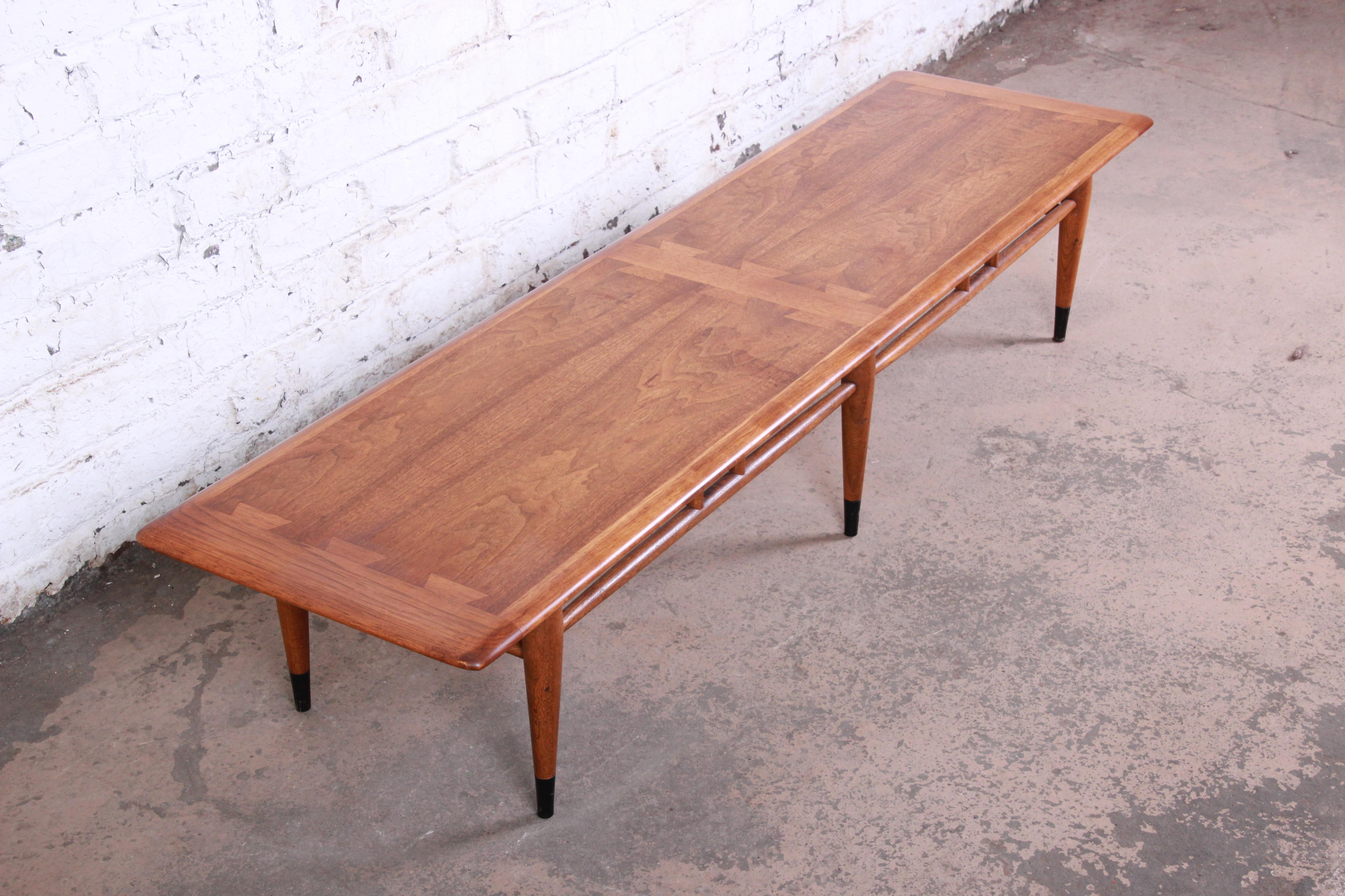 A gorgeous Mid-Century Modern long coffee table from the Acclaim line by Lane. The table features beautiful walnut and ashwood grain and a unique dovetail design. It sits on tapered legs with ebonized feet and sleek stretchers connecting the legs.