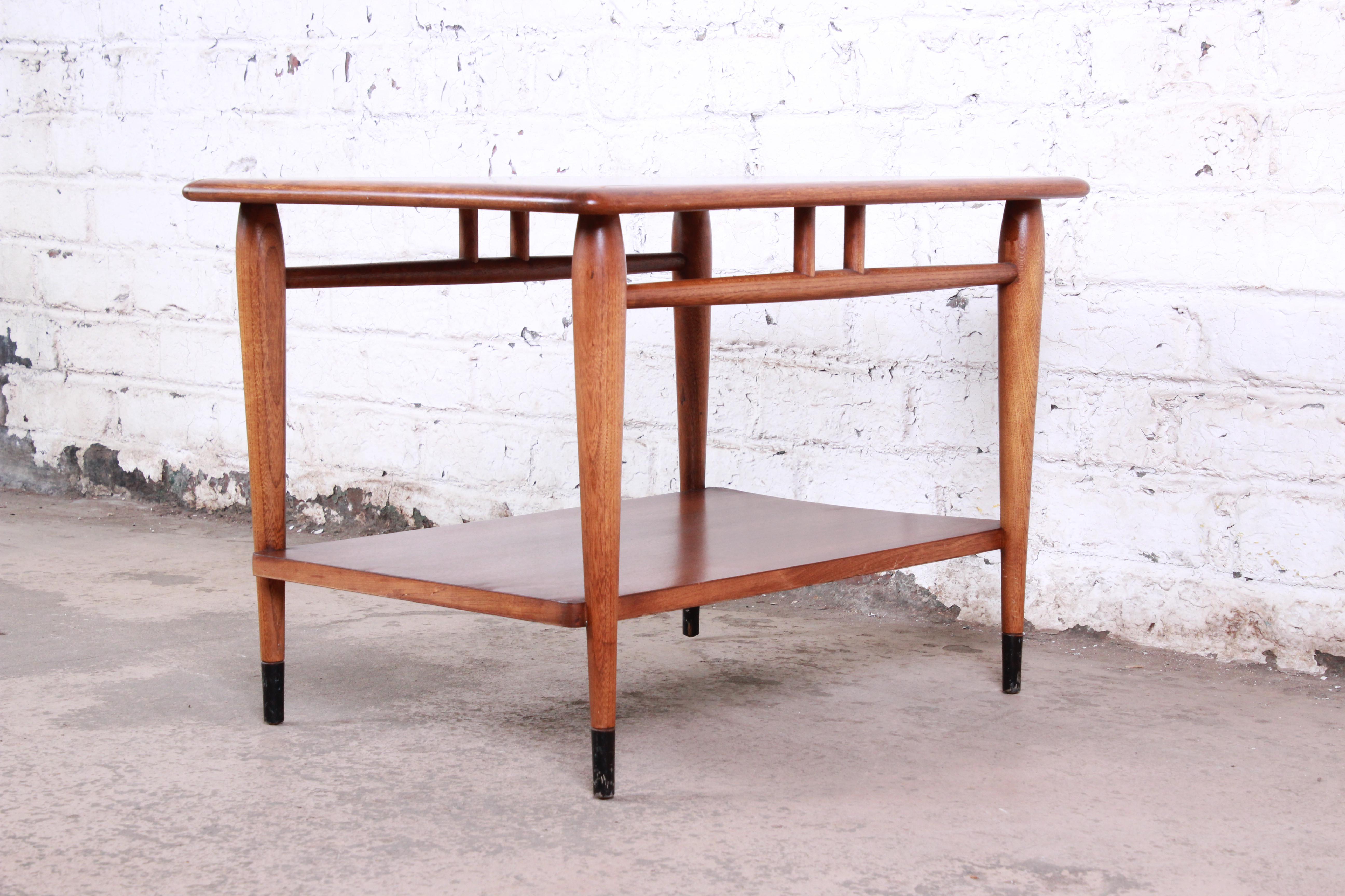 A gorgeous Mid-Century Modern side table from the Acclaim line by Lane. The table features beautiful walnut and ashwood grain and a unique dovetail design. It sits on tapered legs with ebonized feet and sleek stretchers connecting the legs. The