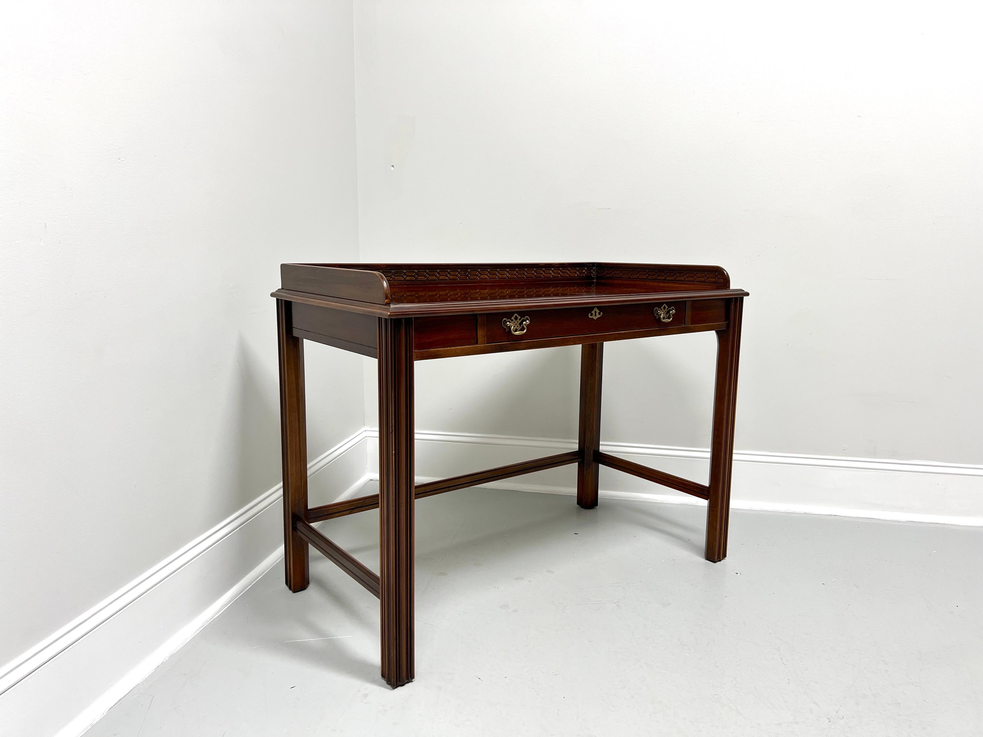 A Chippendale style writing desk by Lane Furniture. Mahogany with brass hardware, a banded bookmatched top with an ogee edge, decoratively carved gallery, stretchers, and fluted straight legs. Features one large center drawer of dovetail