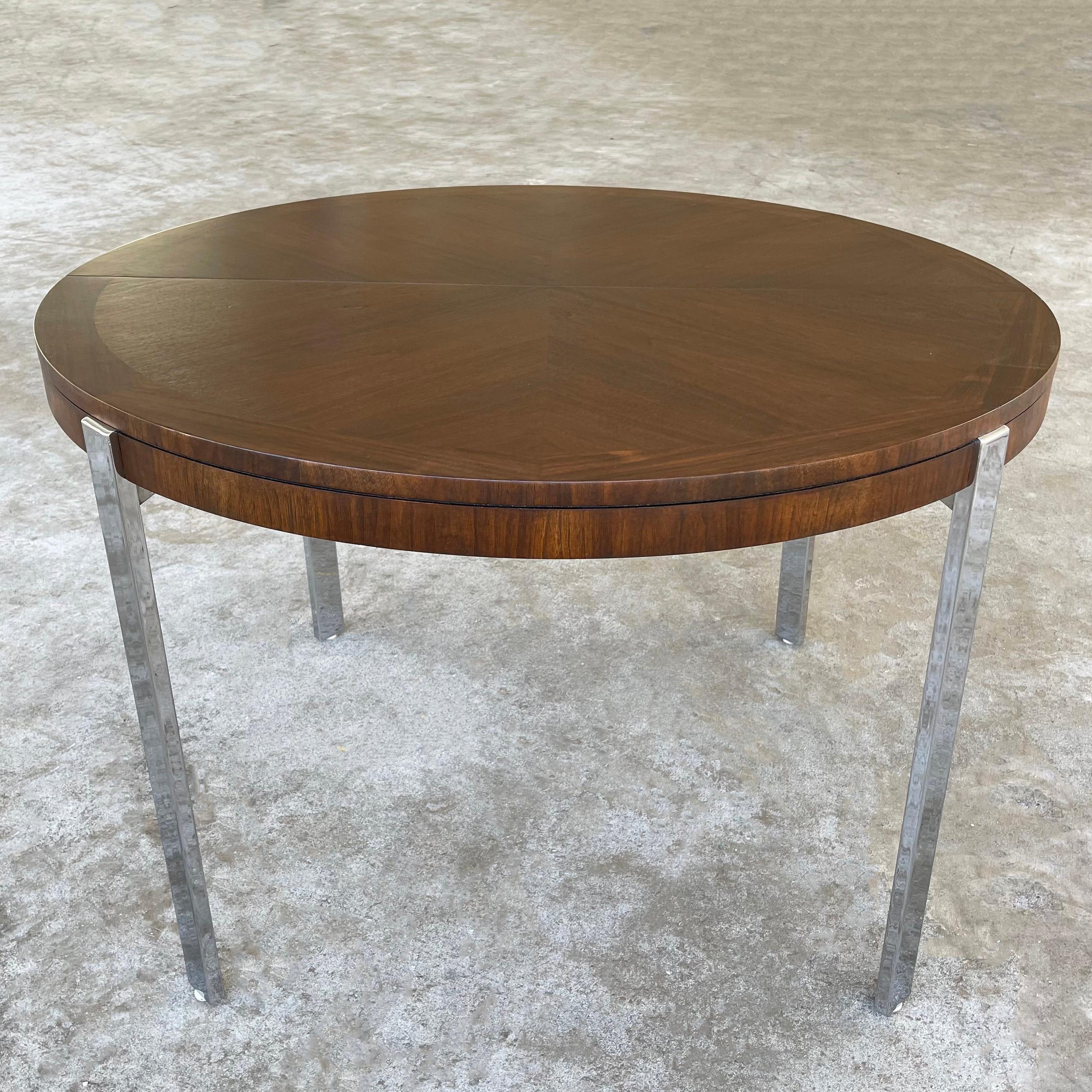Sleek, mid-century modern, round, extension dining table by Lane Alta Vista features a bookmatched walnut top with contrasting trim on flat bar chrome legs. It's a wonderful combination of materials and subtle design elements. The table extends to
