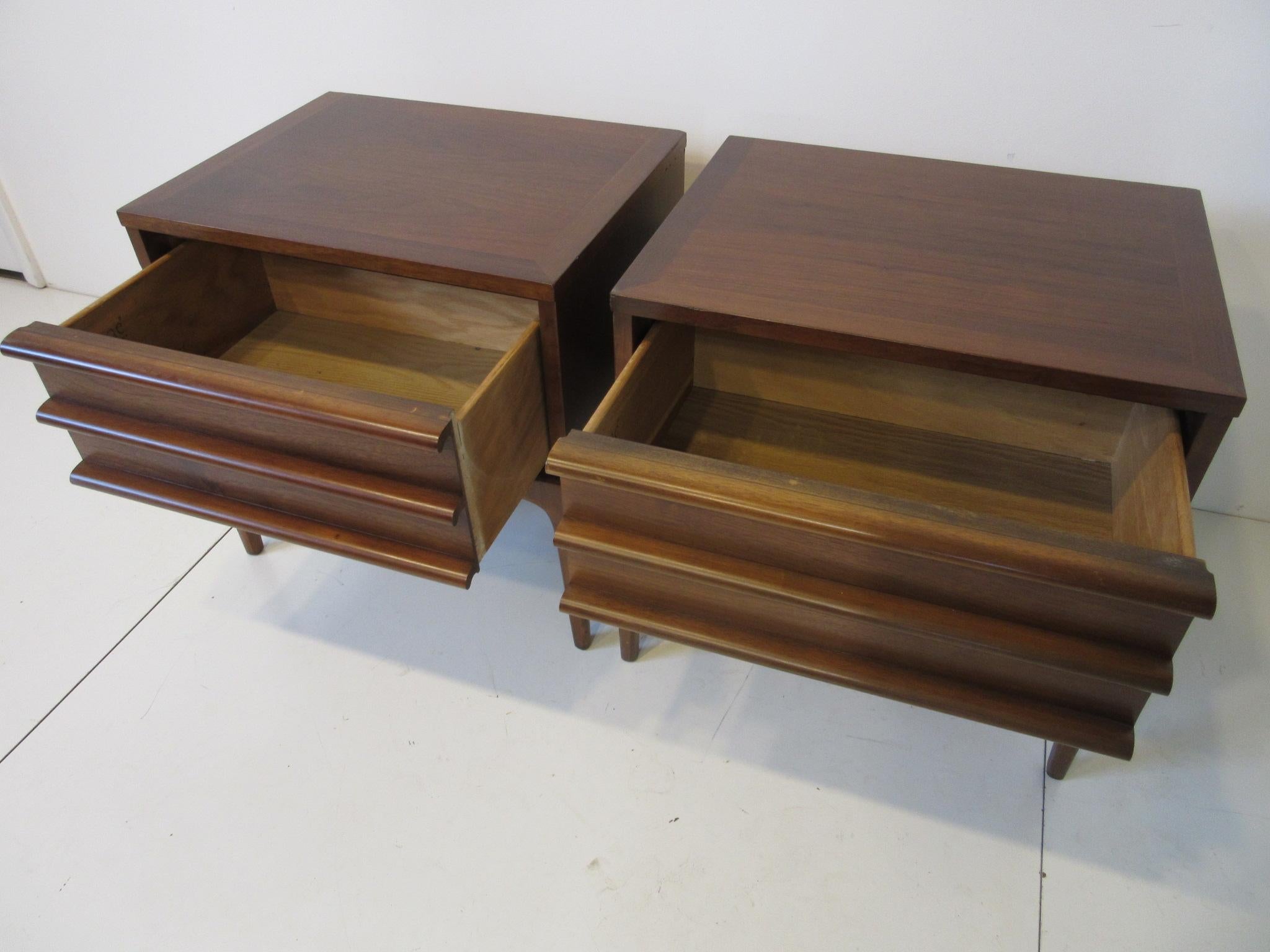 A pair of walnut Minimalist nightstands / end tables with drawers sitting on simple slender legs for a light feel, manufactured by the Lane Altavista Furniture company from their Rhythm collection. These nightstands can be matched with any type of