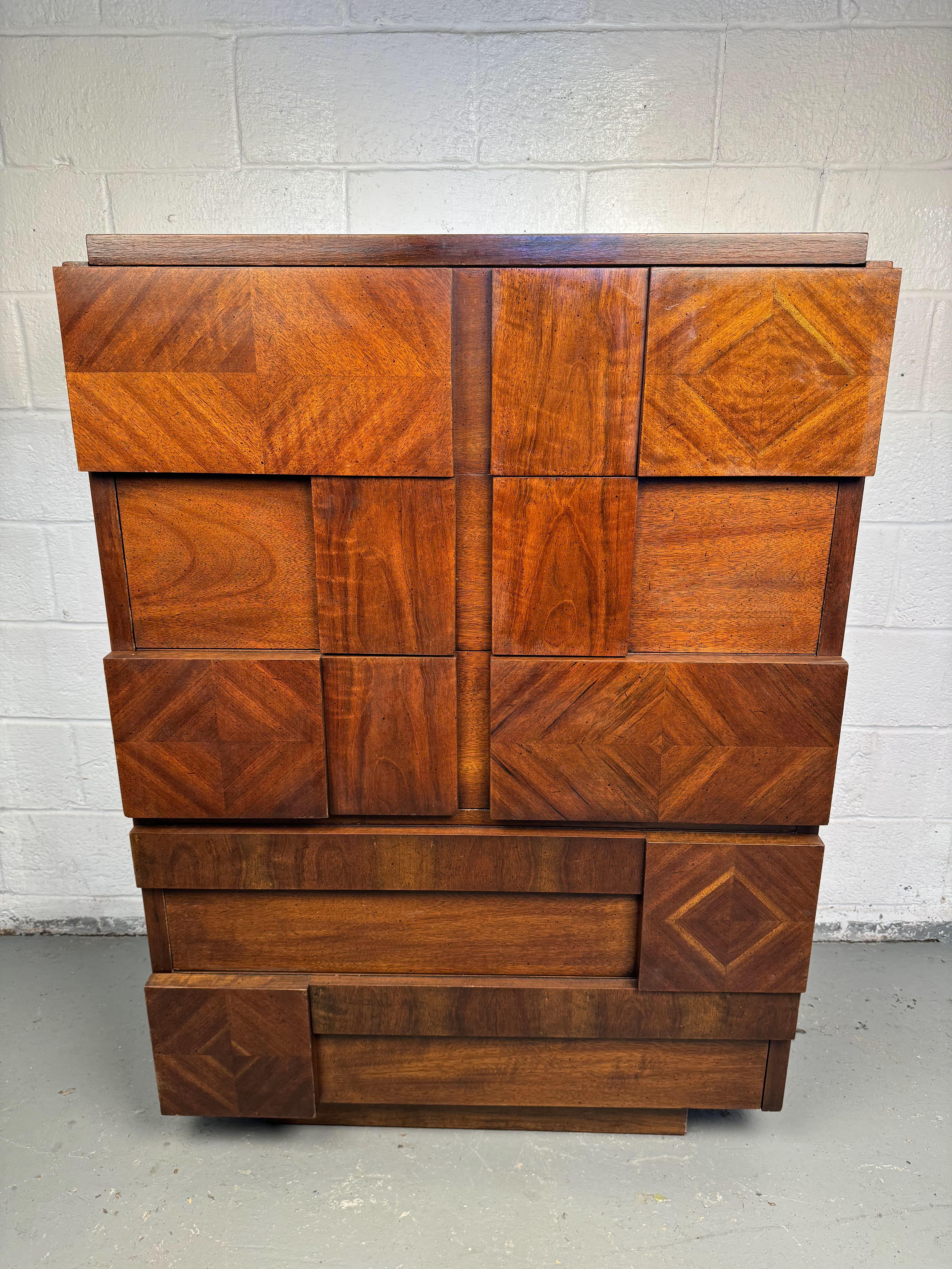 This striking Lane Staccato highboy dresser is a quintessential example of the Brutalist style that characterized much of mid-century modern design during the 1970s. Crafted from robust, richly hued wood, this dresser features a distinctive,