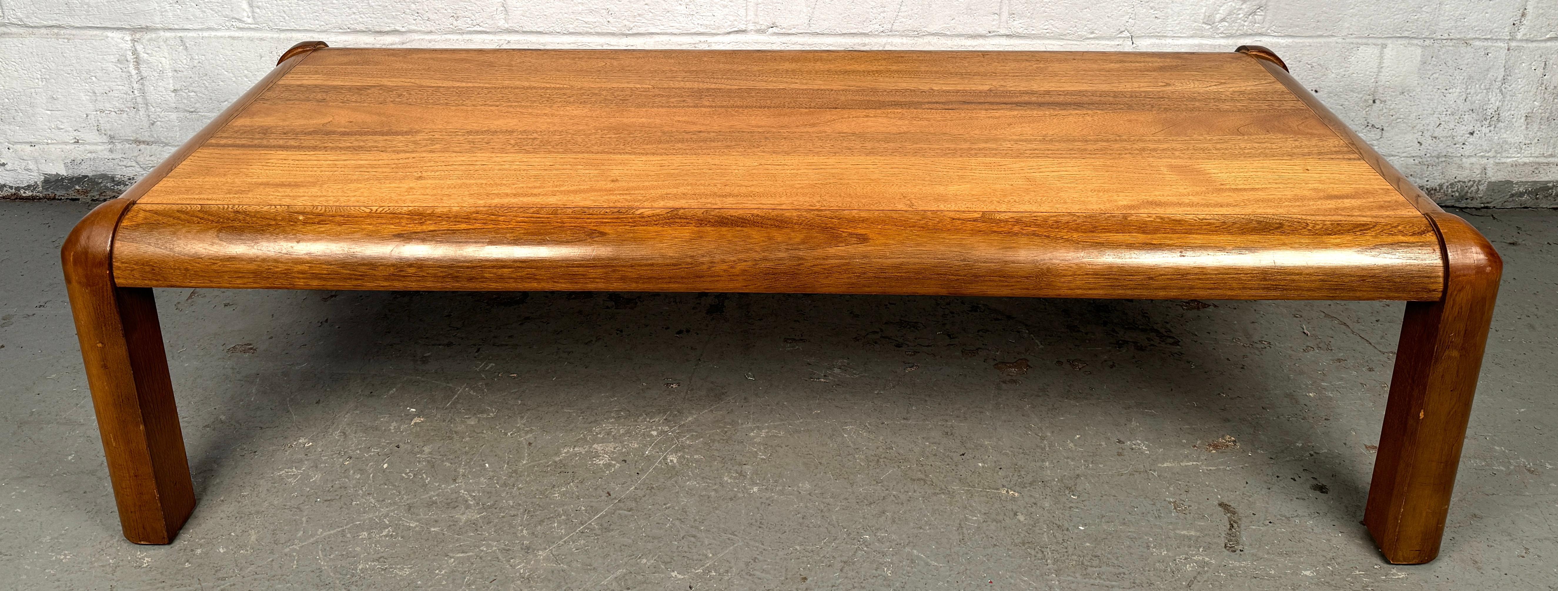 Une étonnante table basse moderne du milieu du siècle par Lane, fabriquée à partir de teck riche avec des bords magnifiquement arrondis qui adoucissent son design épuré et minimaliste. Le grain de bois lisse et chaud et les pieds subtils et effilés