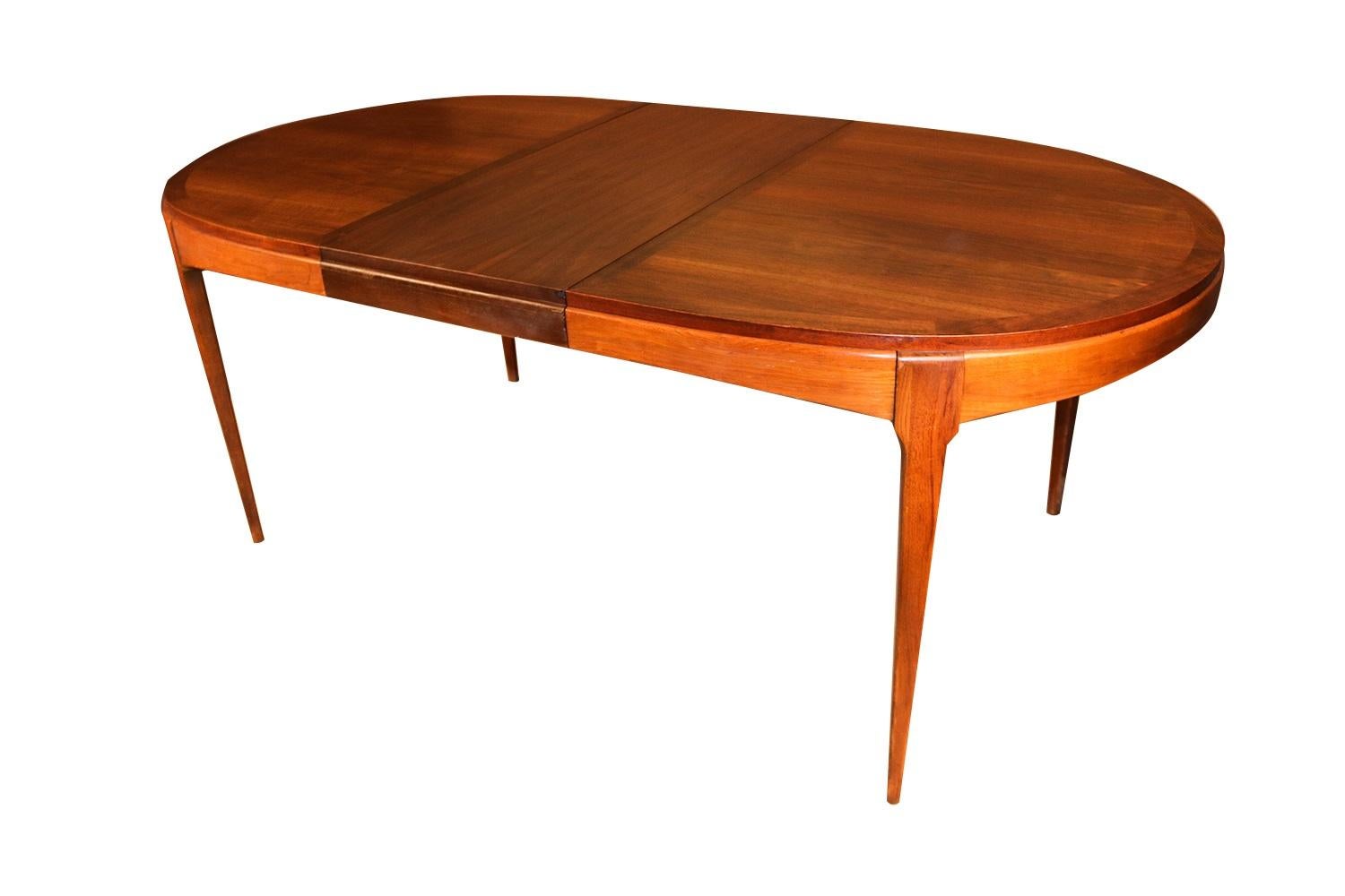 Beautiful Mid-Century Modern expandable, Lane First Edition dining table, manufactured by Lane. Features an oval shaped top accented with richly grained, walnut, clean lines characteristic of Classic Danish design. Raised over four tapered legs,