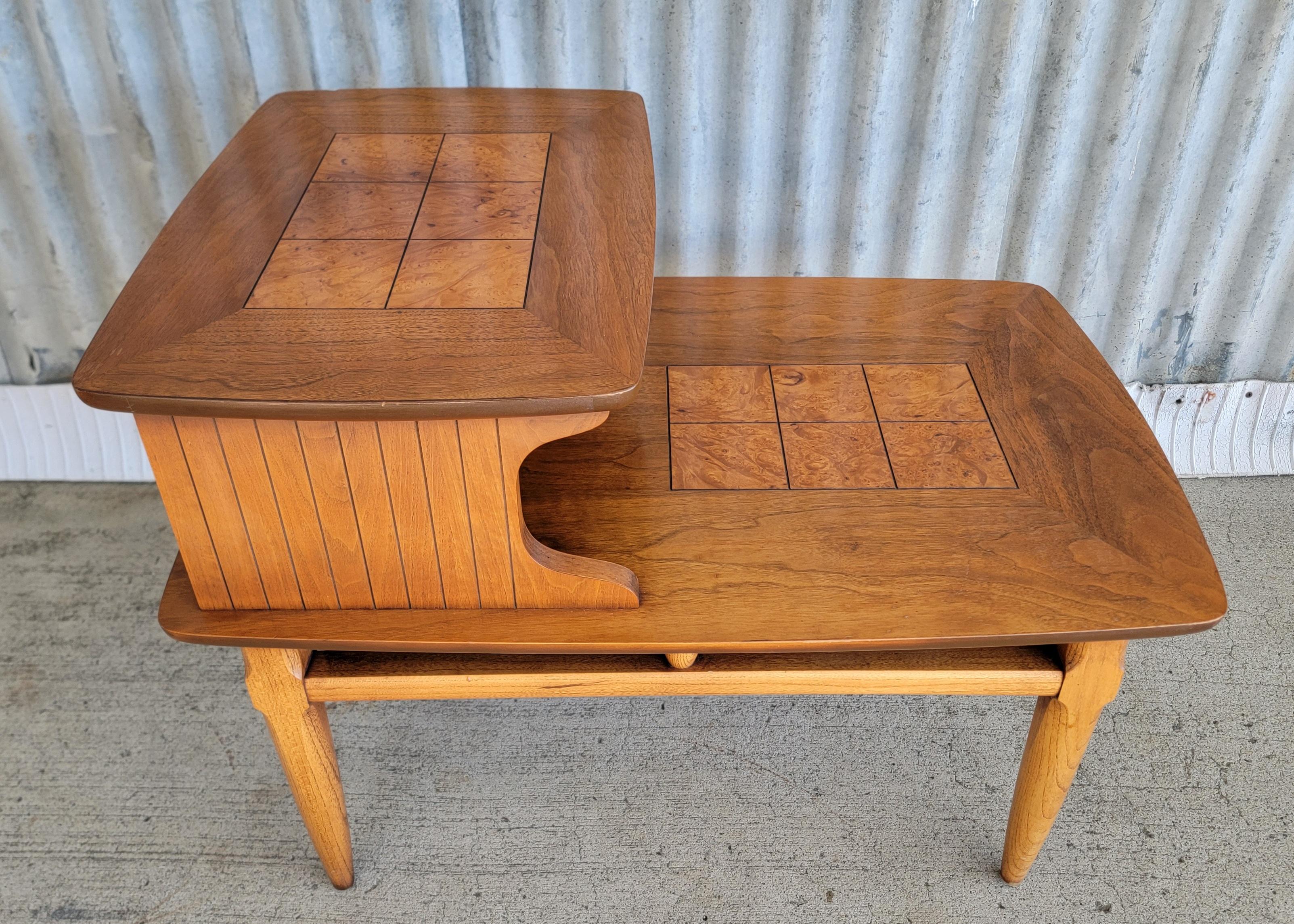 A Mid-Century Modern 2 tier or step end table by Lane Furniture. Circa. 1960. Tapered legs with a tile type burl-wood detail. Very good original condition with original finish. Lower table top measures 14.75 inches high. 