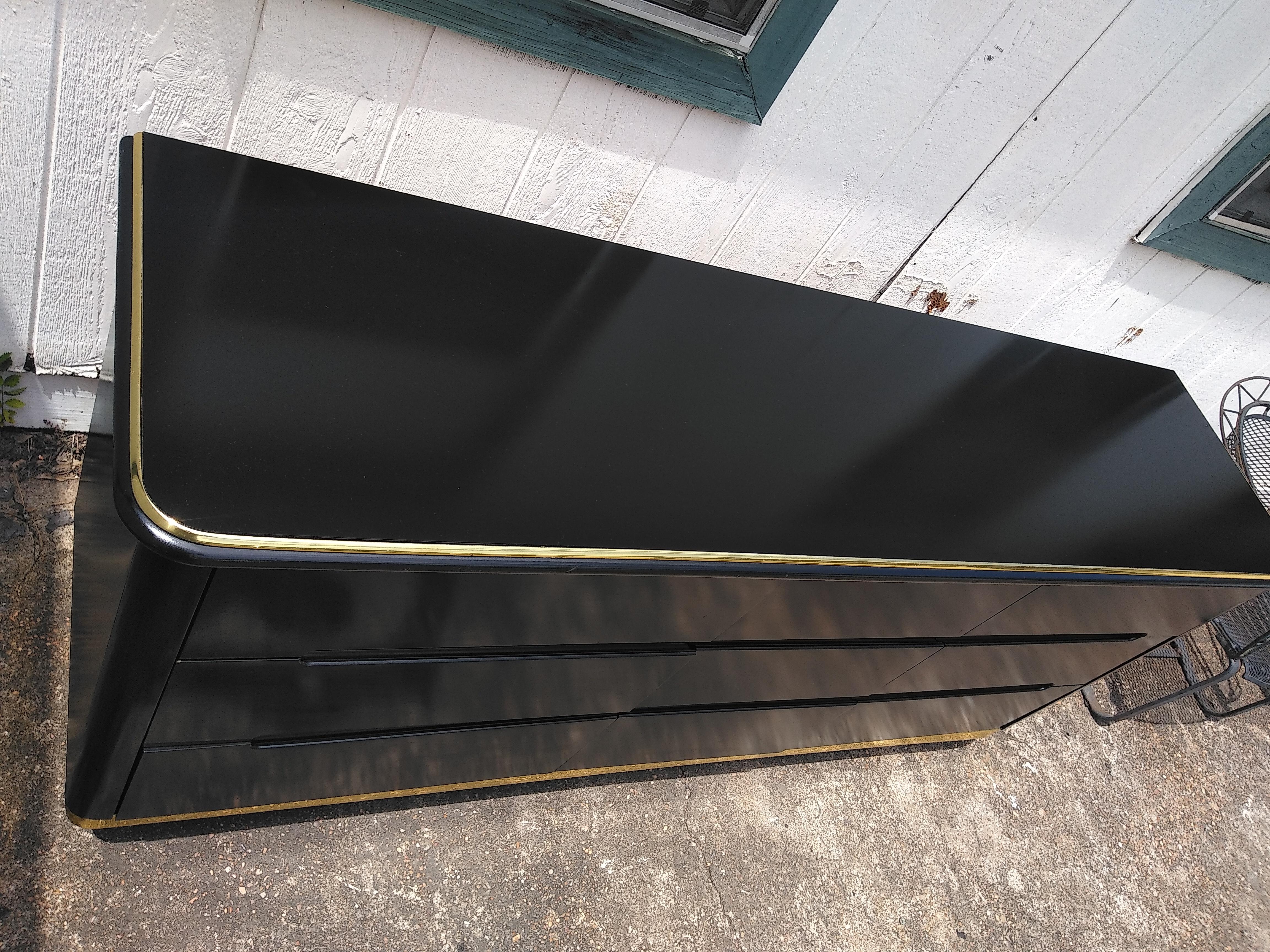 This is a stunning 9 Drawer Dresser by Lane Furniture. It's made of wood and has a black lacquer finish with brass accents.  It  has 9 drawers for plenty of storage. It has an Art Deco Waterfall look. It sits on a brass accents plinth base  and