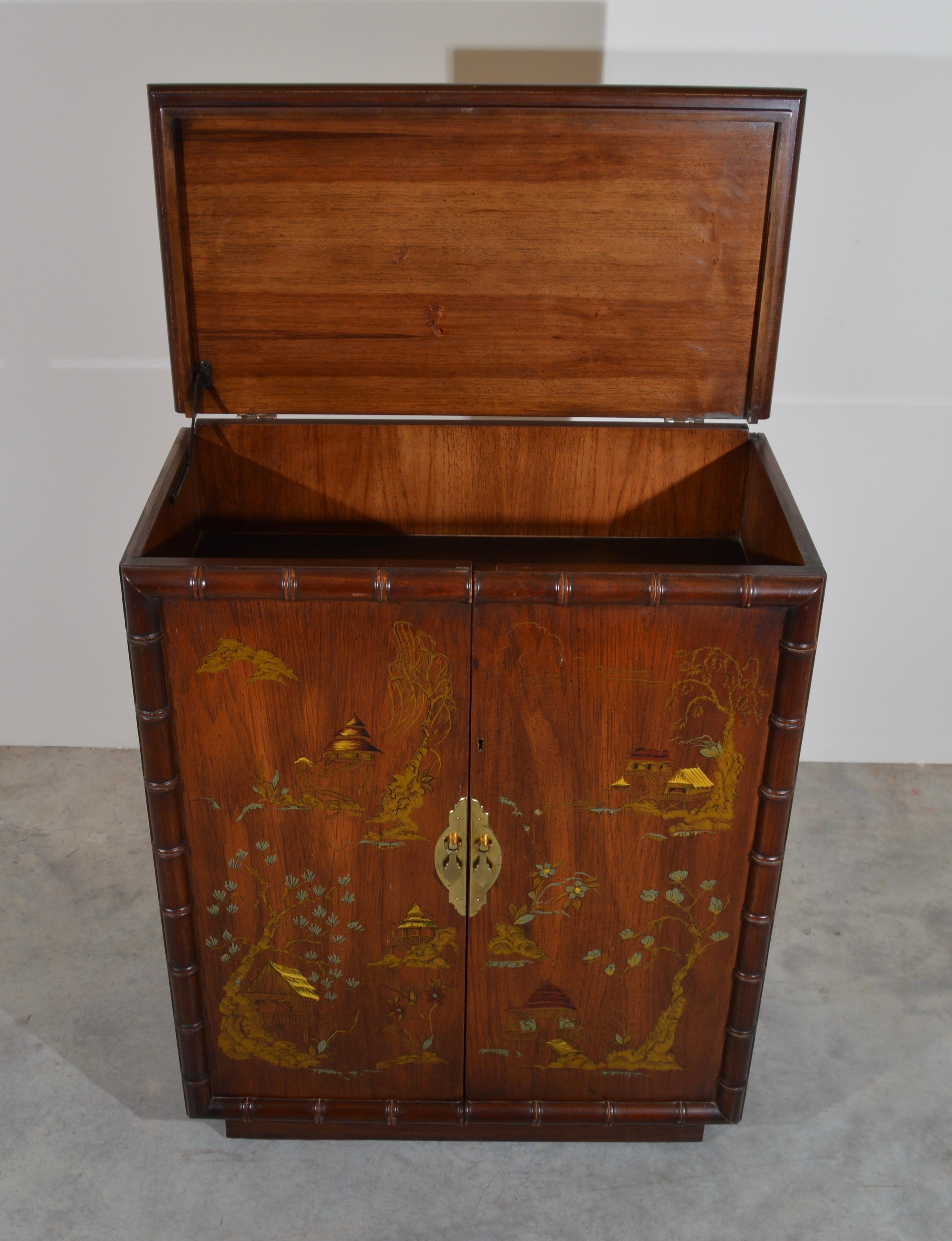 A midcentury bar cabinet having faux bamboo features with hand painted doors. The top flips up and is braced by a locking arm to allow bottle service. Ample storage underneath having one shelf and high storage for glasses and when your bottles are