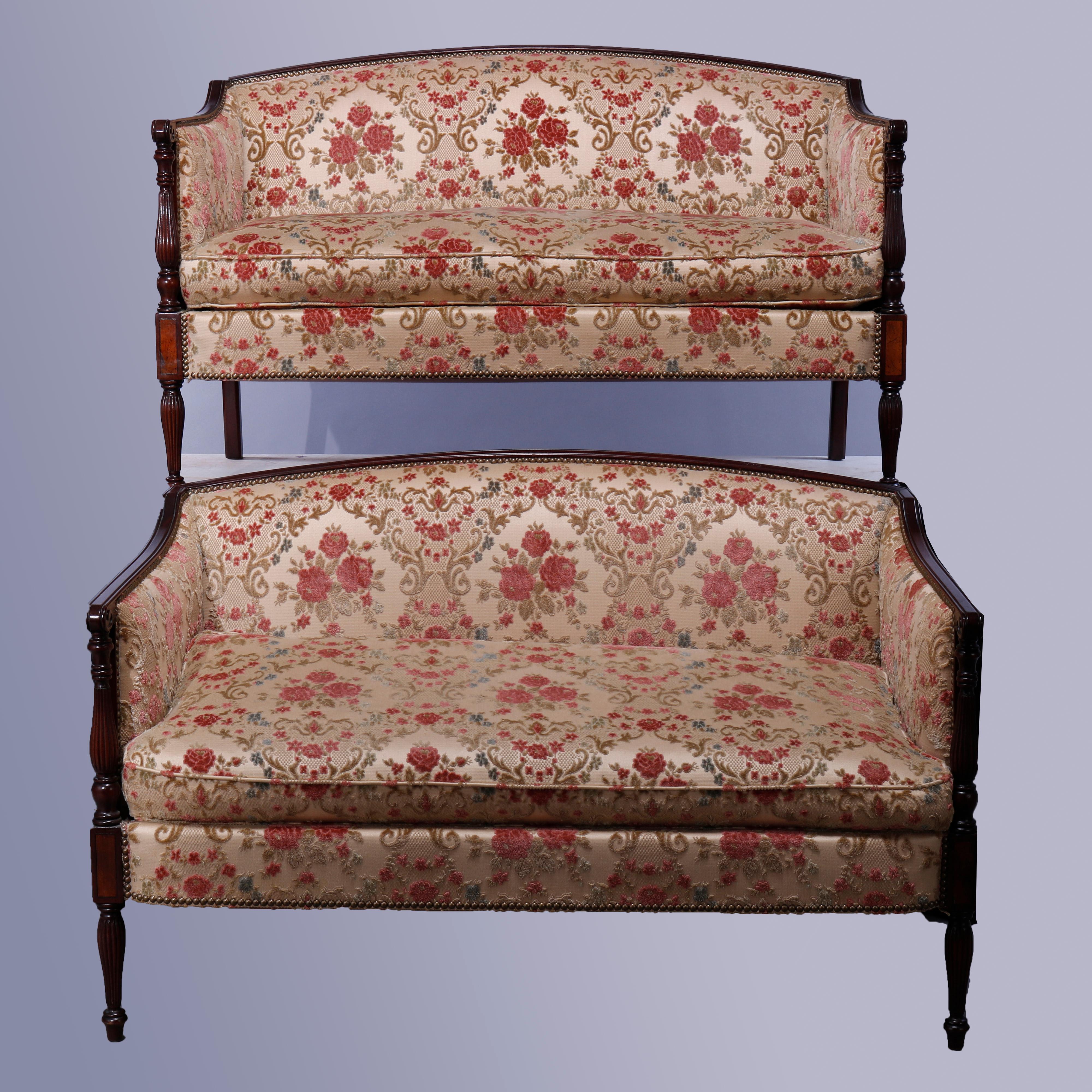 An antique pair of matching Sheraton style settees by Lane Hickory Chair Co. offer mahogany construction with arched backs surmounting upholstered backs and seats flanked by scroll form arms with turned and reeded balustrade supports with satinwood