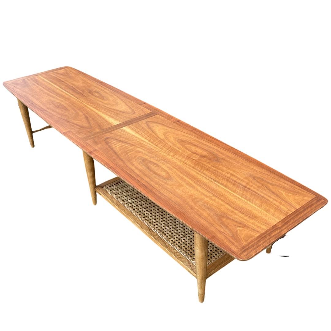 Vintage-modern American made coffee table, features one drawer with a carved pull, one cane shelf, sculpted legs and beautiful walnut grain, manufactured by Lane.