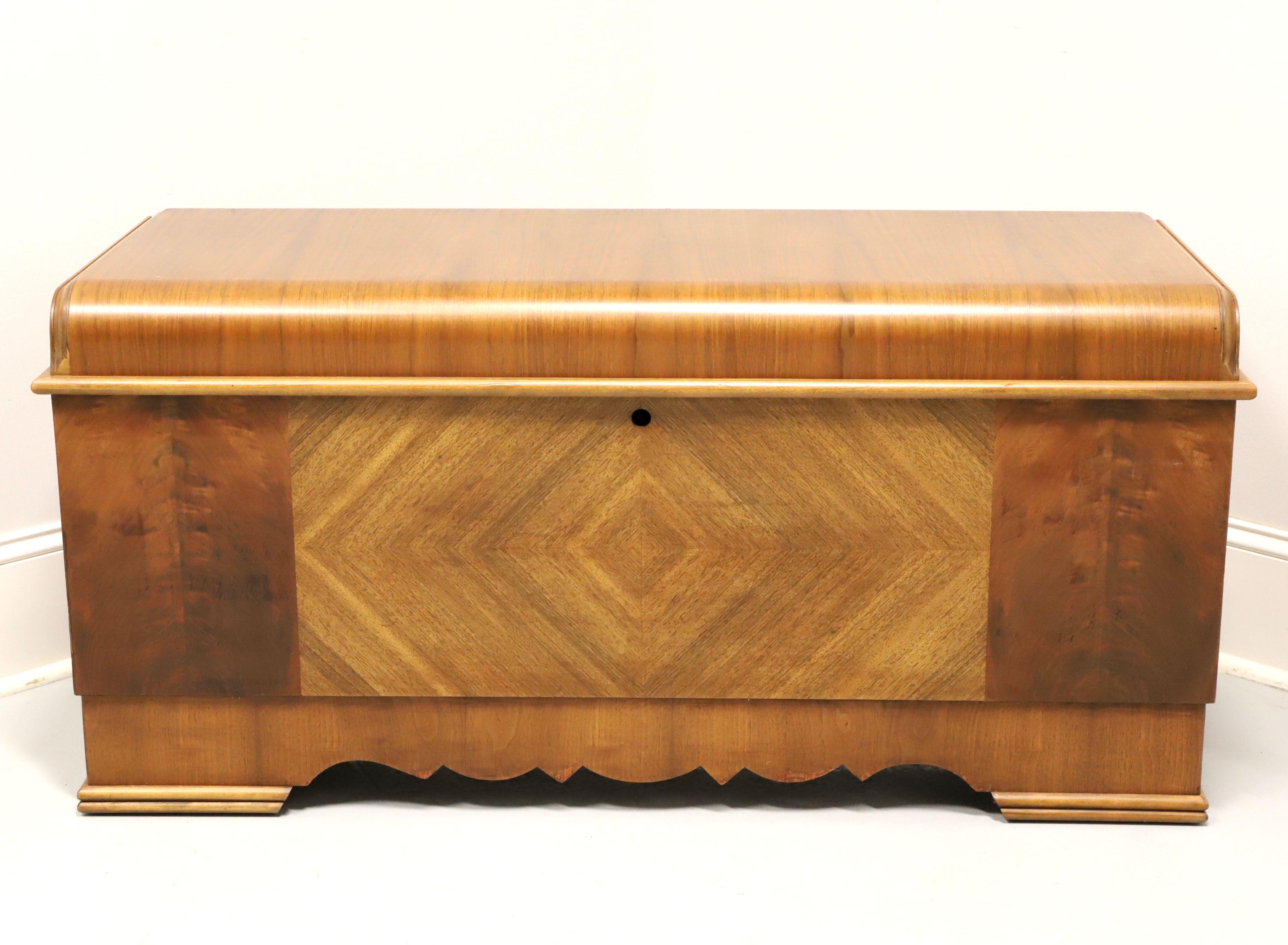 An Art Deco style cedar chest by Lane. Walnut with inlaid parquetry veneers, rounded lid, metal hinge hardware, cedar lined interior, a hinged upper felt lined divided storage tray and decoratively carved apron. Does NOT lock or latch, as required