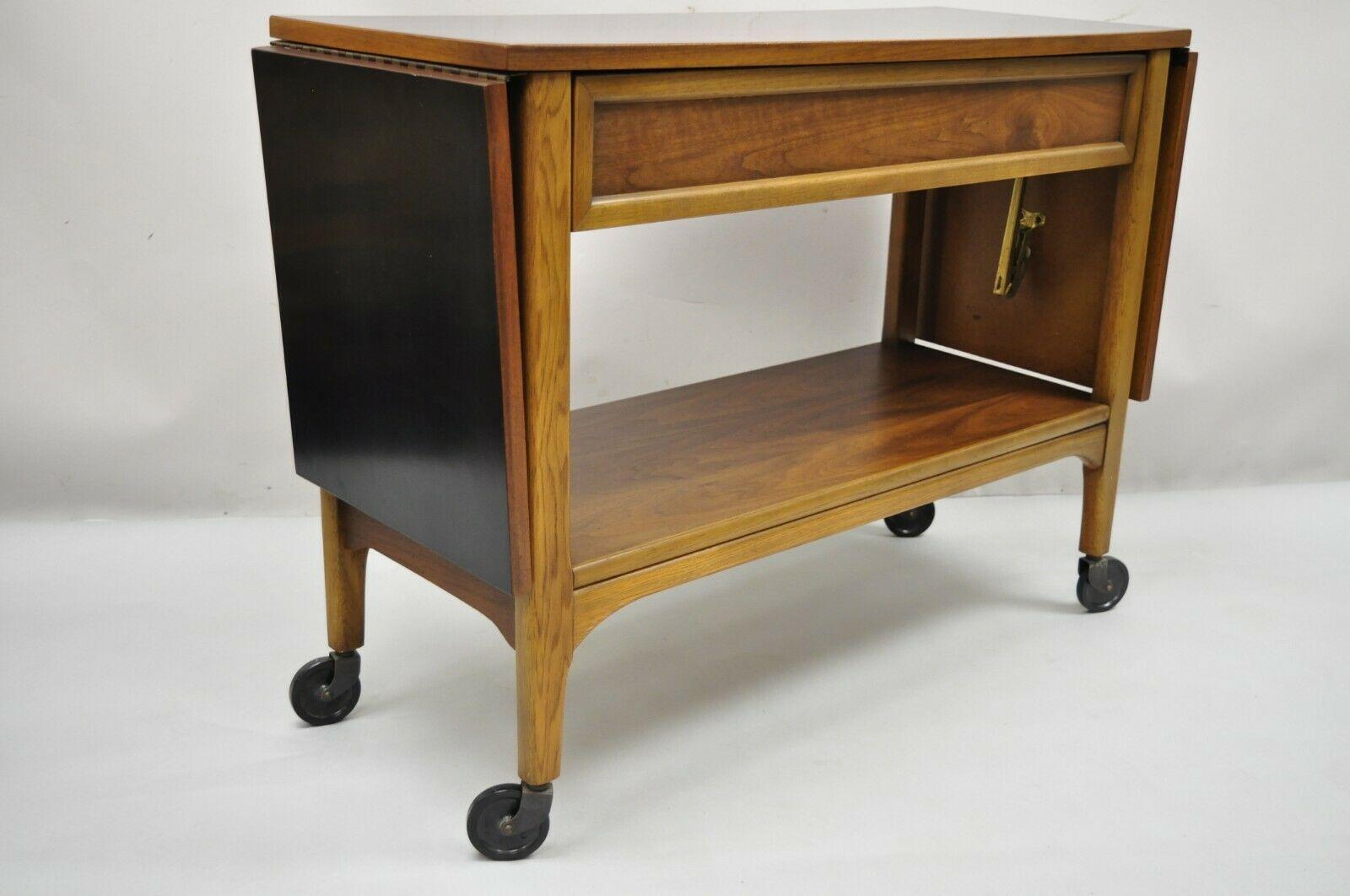 Lane Mid Century Modern Walnut Modern One Drawer Drop Leaf Rolling Bar Cart. Item features drop leaf sides, rolling casters, black laminated top,1 dovetailed drawer, finished back, clean modernist lines, quality American craftsmanship. Circa Mid
