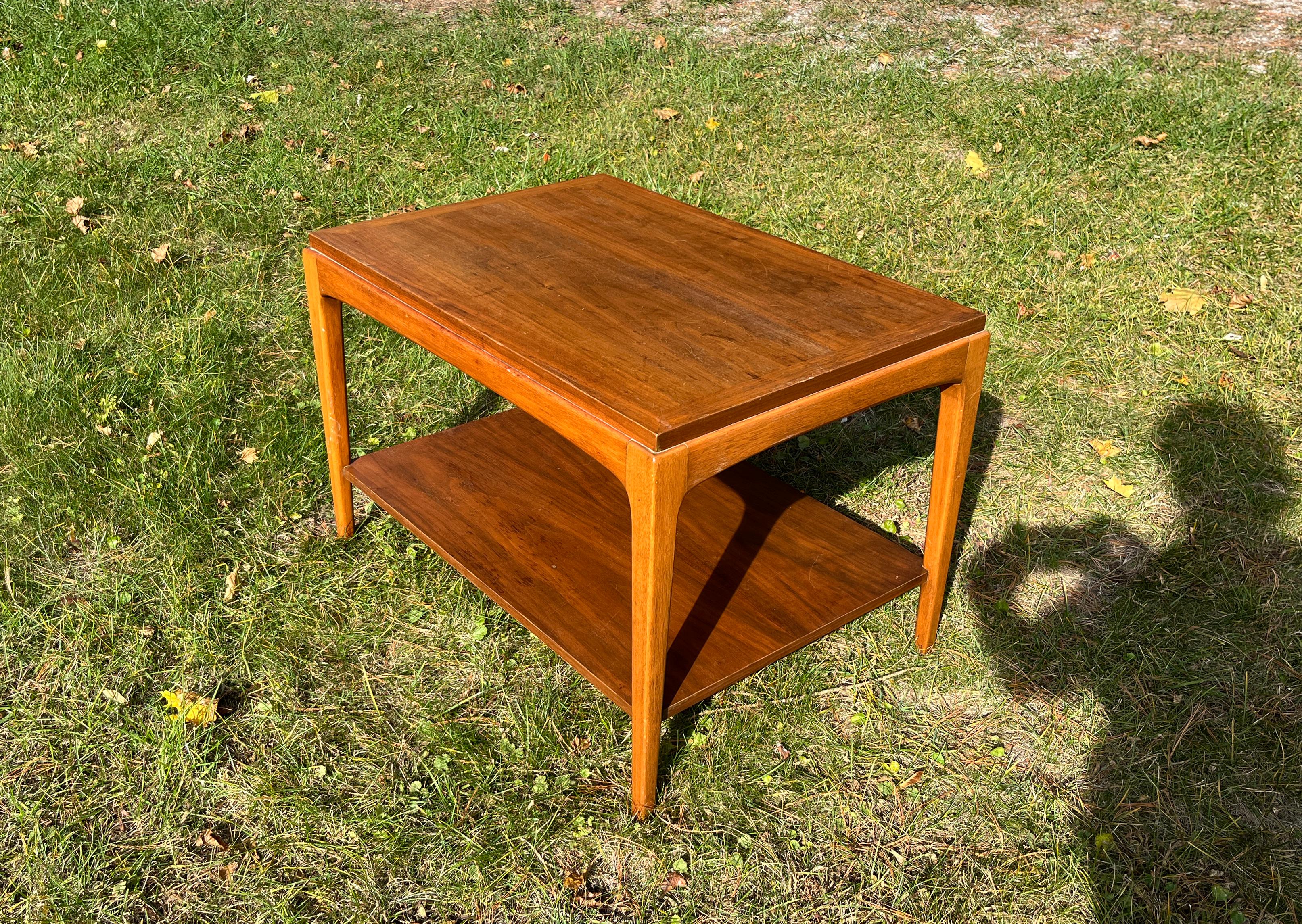 This MCM two-tiered, walnut veneer side table was manufactured by Lane Furniture in the 1960s as part of its Rhythm Collection. The Lane brochure describes this collection as being 