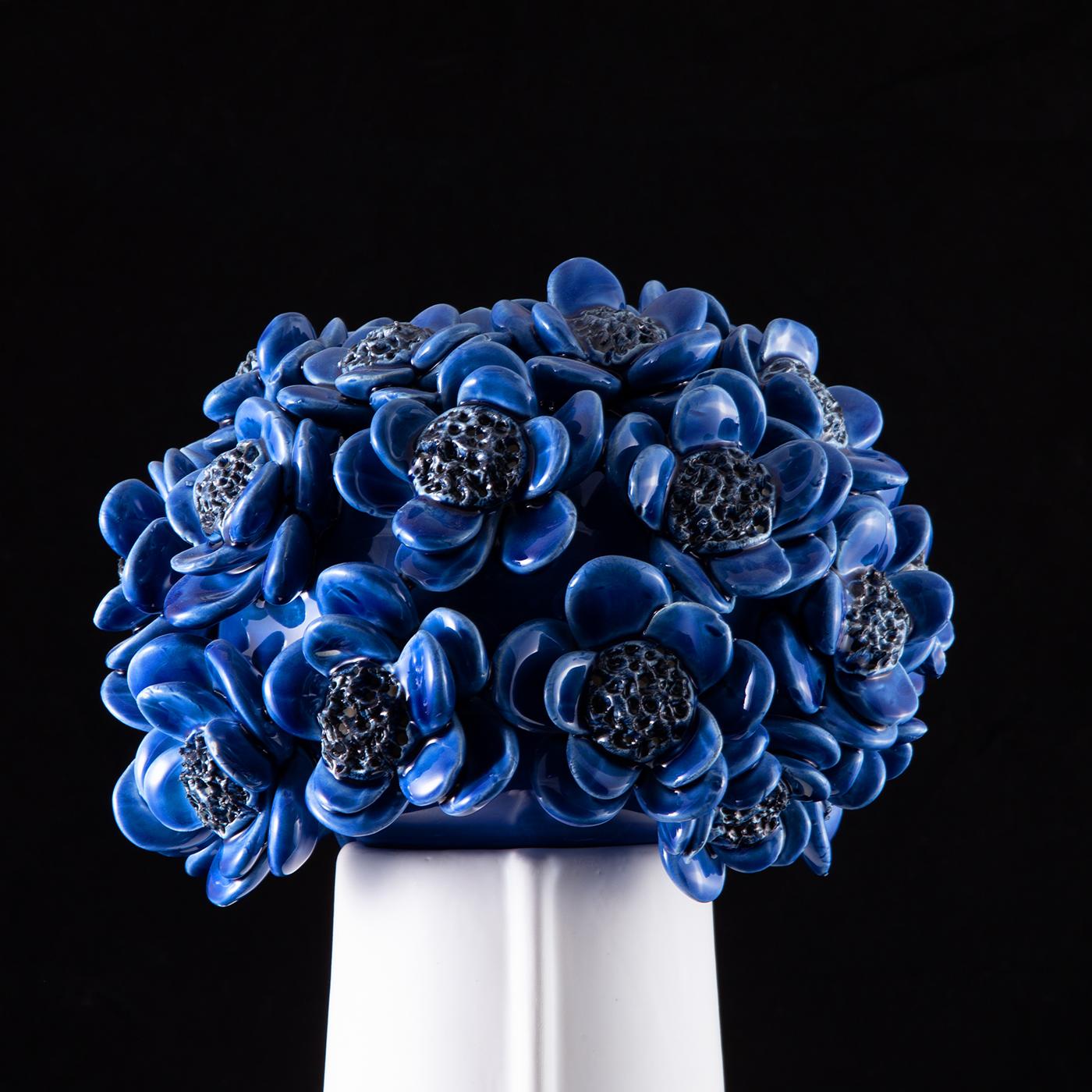 Un couvercle de fleurs de tournesol d'un bleu profond affirme au premier coup d'œil la valeur décorative incontestable de ce motif. Le corps en céramique blanc brillant sur lequel il est posé arbore d'élégants traits anthropomorphiques et dissimule