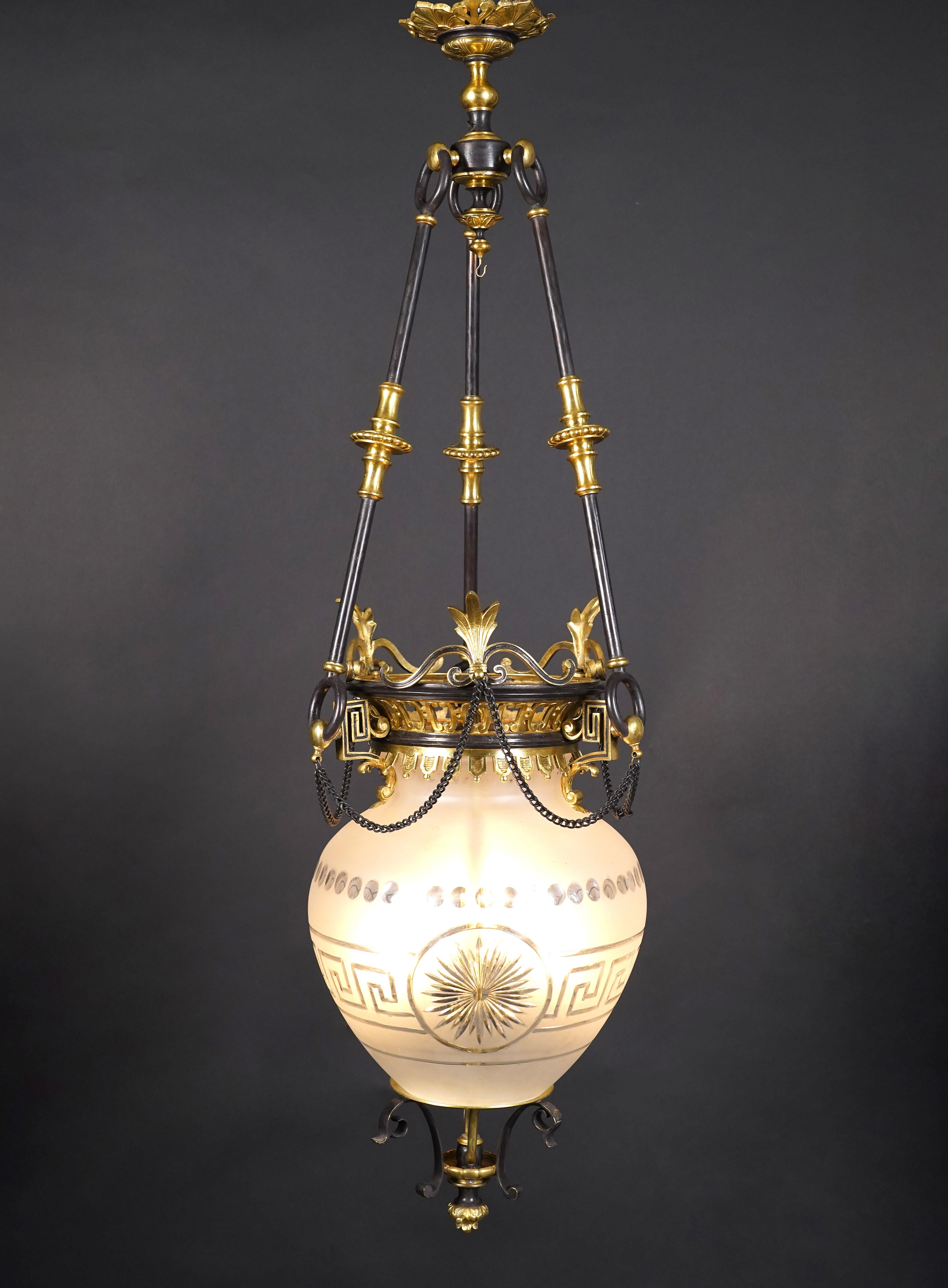 Beautiful lantern in double patina bronze and crystal. The central shaft is engraved with a Greek frieze centered on a star. The whole is suspended from a openwork crown decorated with stylized leaves, from which three uprights end in a ceiling