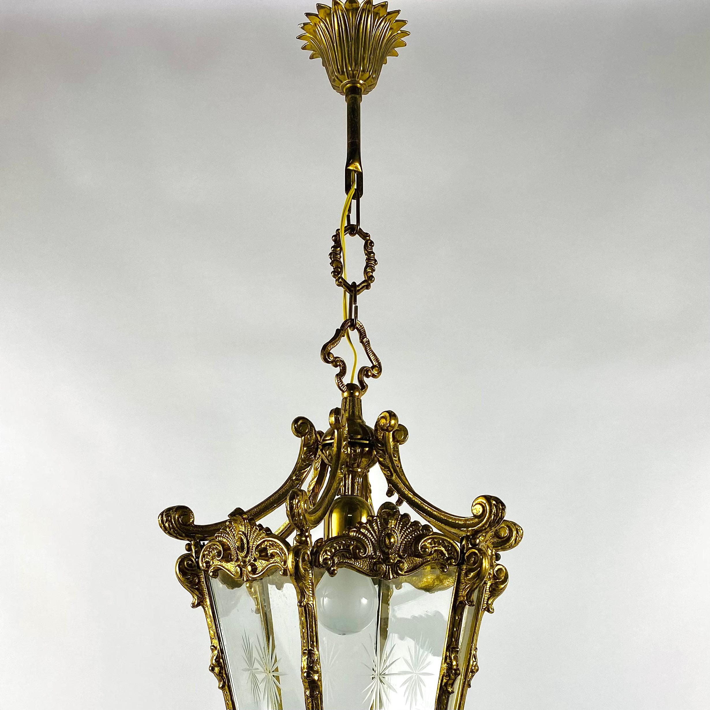 Amazing gilded bronze antique hall lantern with one lamp surrounded by sectional convex tapering glass panels and held within a foliated scrolling framework with decorative central pierced leaves and open scrolling canopy, having the original chain