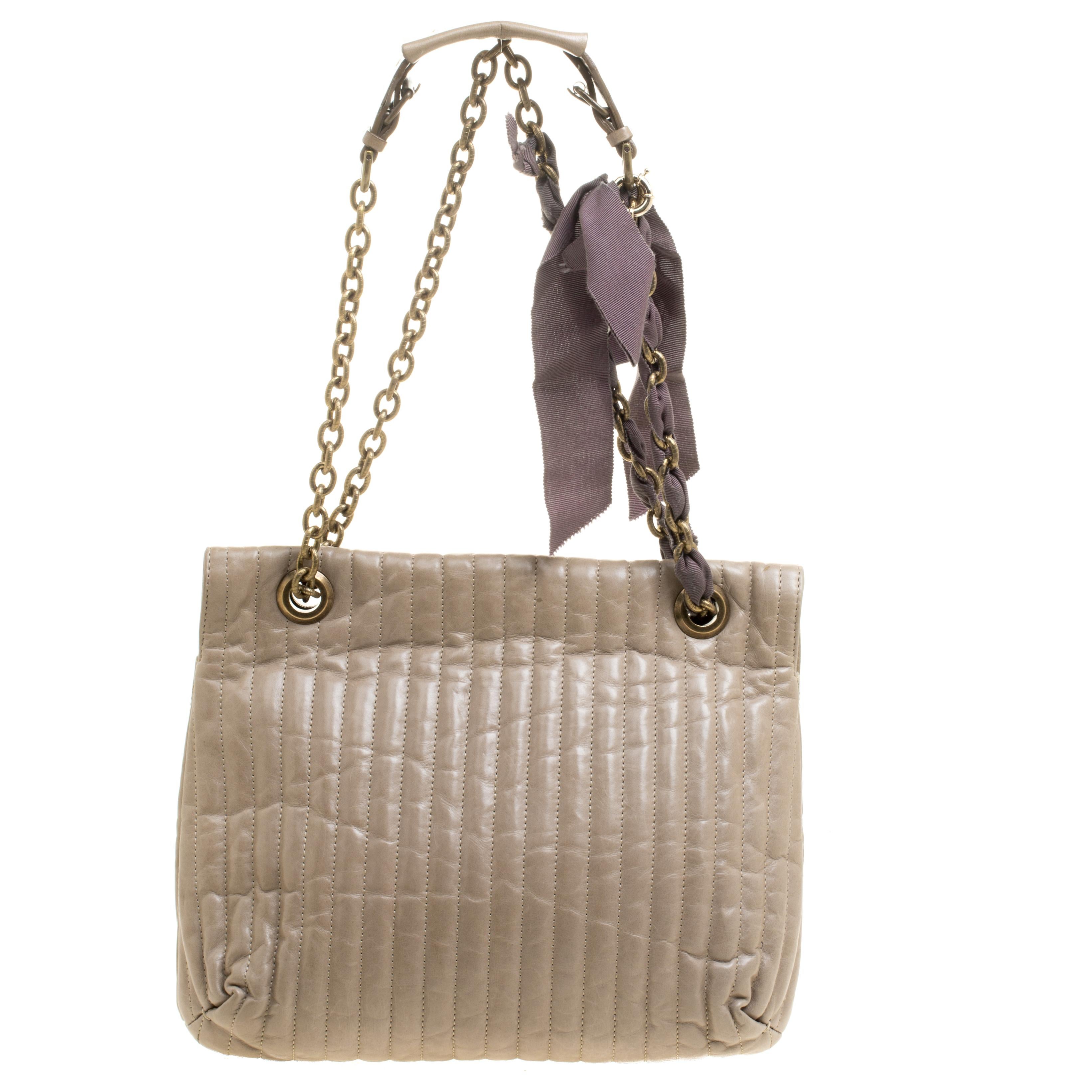 This stylish Happy shoulder bag from Lanvin is crafted from beige leather. The bag features a dual chain link strap with leather shoulder rest and a bow detail. The turn lock closure opens to a spacious fabric lined interior that houses a zip pocket