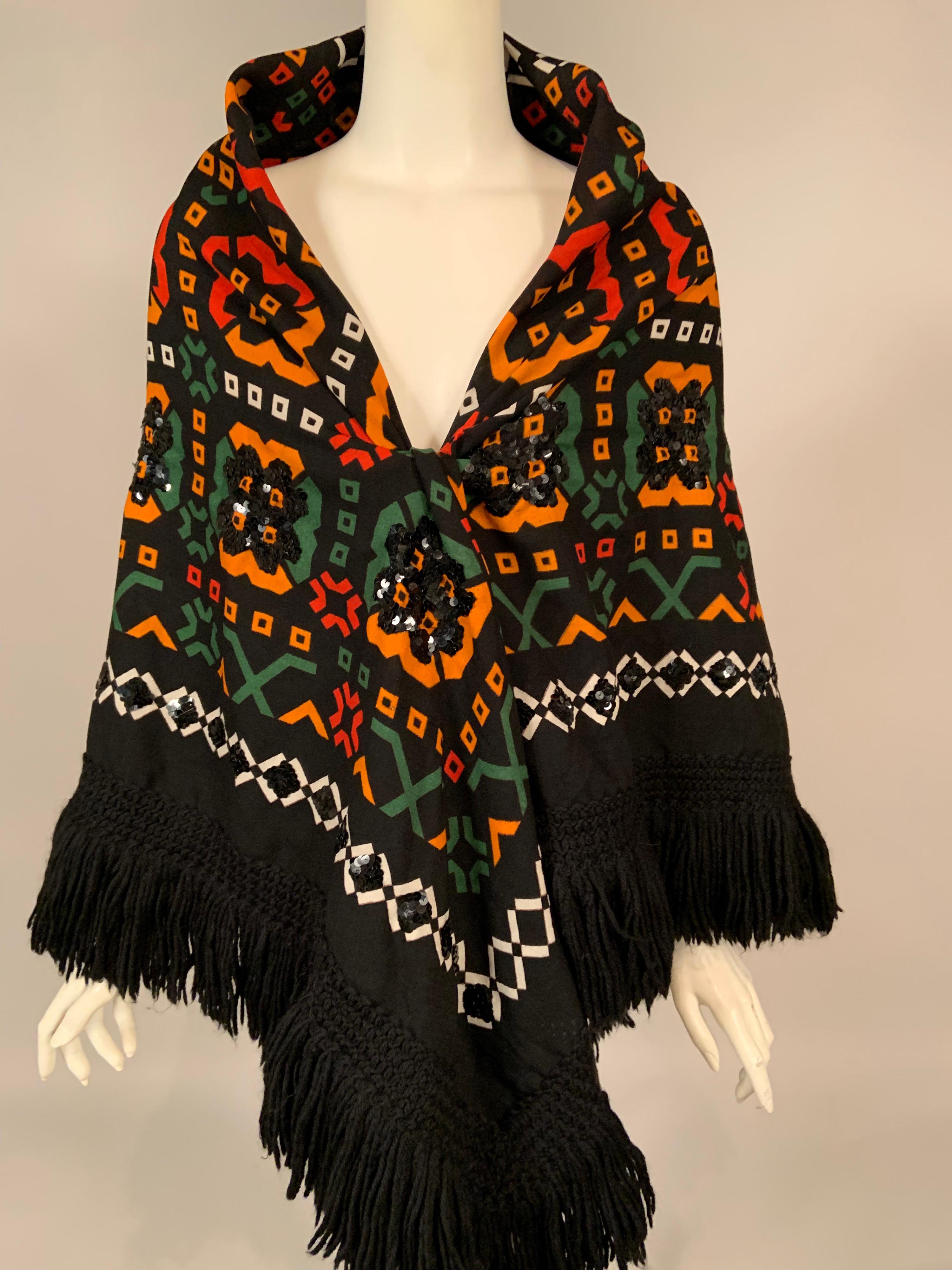 The black wool challis background of this 1970's Lanvin shawl sets off the colorful geometric designs beautifully. There is a white border and contained within this are designs in green, pumpkin, and rust. The shawl has black sequins hand sewn onto