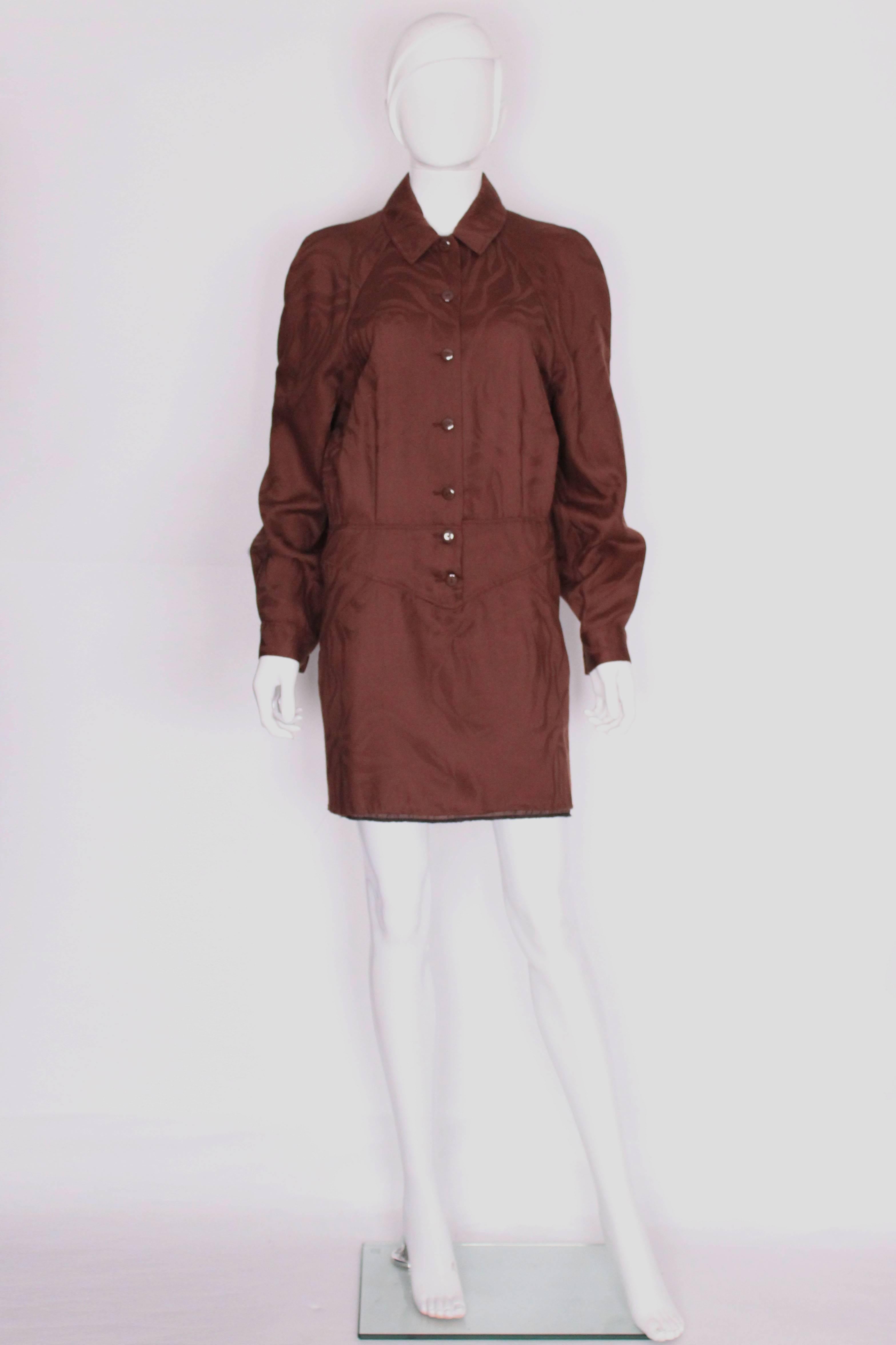 This shirt dress by Lanvin, Paris is in a brown wool printed fabric. It has a shirt collar, with a band detail at the waist. It has a 7 button front opening, button cuffs, 2 slant pockets at waist level, and pleat detail at the back.
