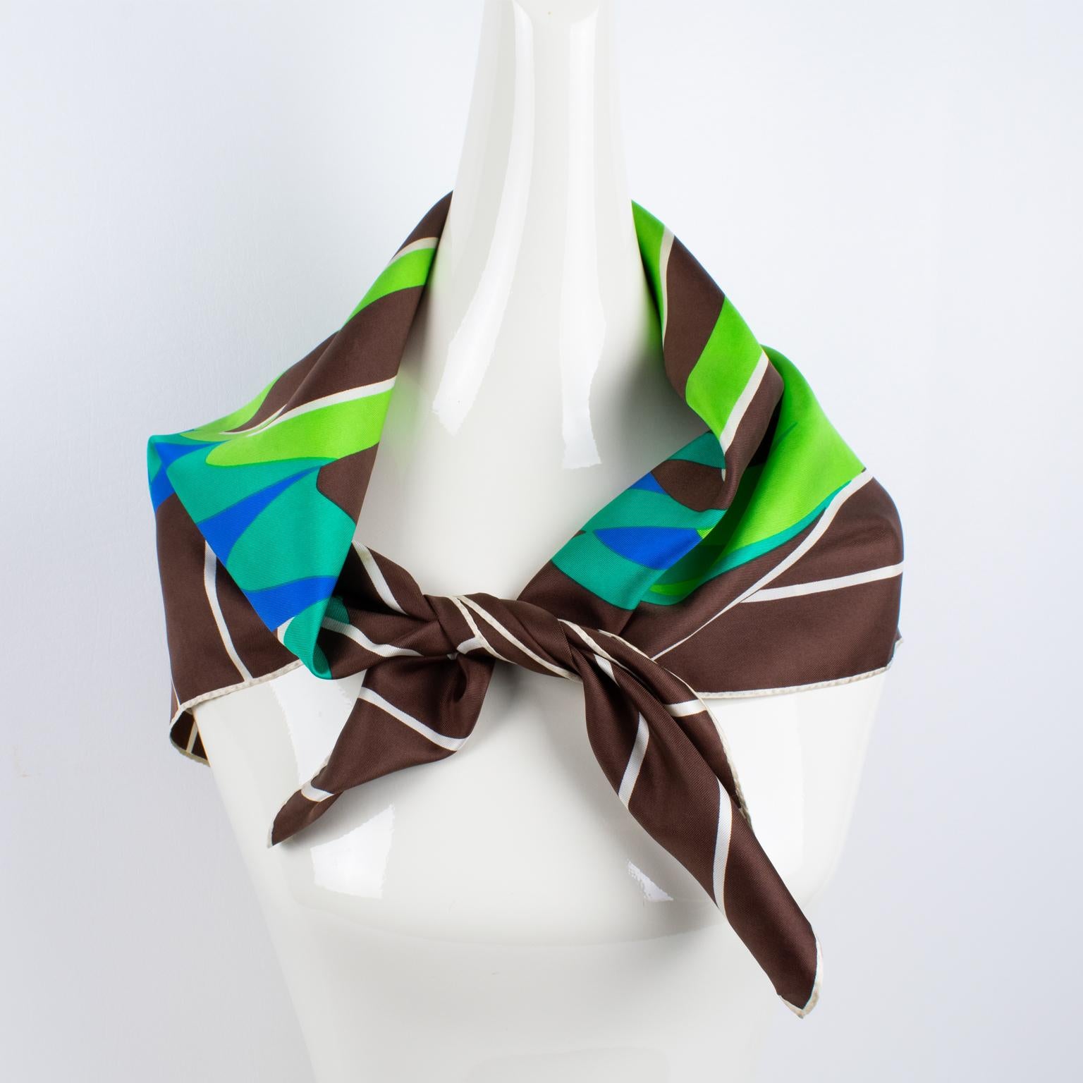 This elegant silk scarf by Lanvin Paris features a typical 1970s geometric optical print pattern. The combination of colors is bright and vibrant, with seafoam green, lapis blue, and turquoise teal over a striped white and cocoa brown background.