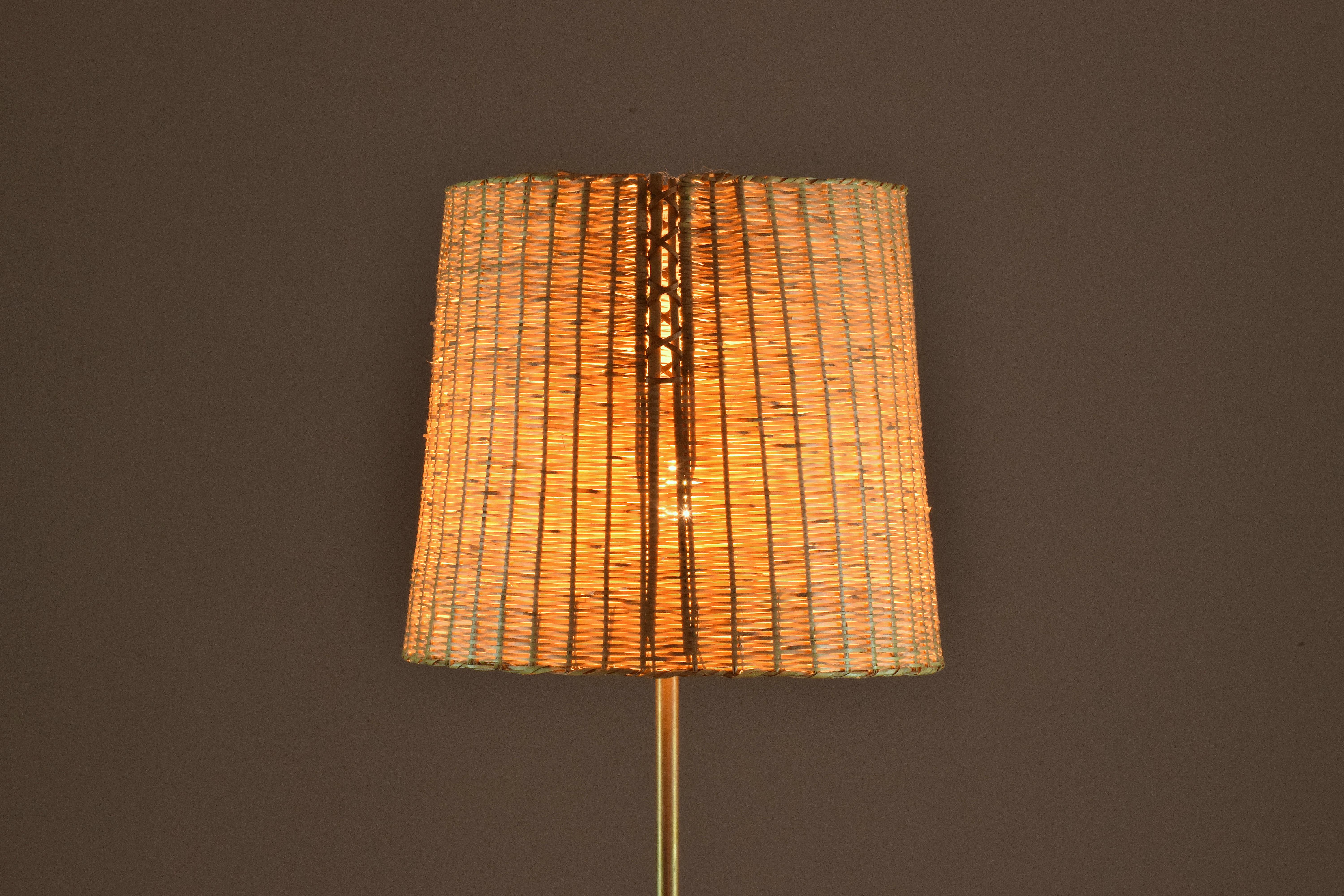 The Ancora floor light stands on an entirely leather sheathed slender brass structure and sits on a tripod solid brass with walnut endings. The shade is delicately handcrafted by expert Moroccan artisans in wicker (or rattan) and features a braided