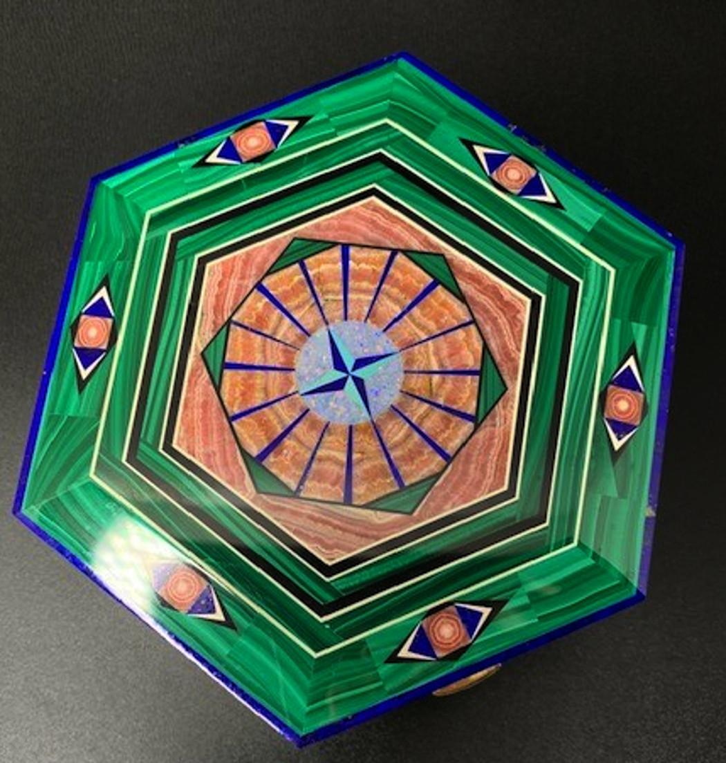  Lapis, malachite,  rhodochrosite, agate, turquoise,  mother-of-pearl and  jasper are all inlaid in this magnificent box. It is hexagonal in shape and decorated with geometric designs. It has a Kalahari jasper interior with 18 karat gold edges and