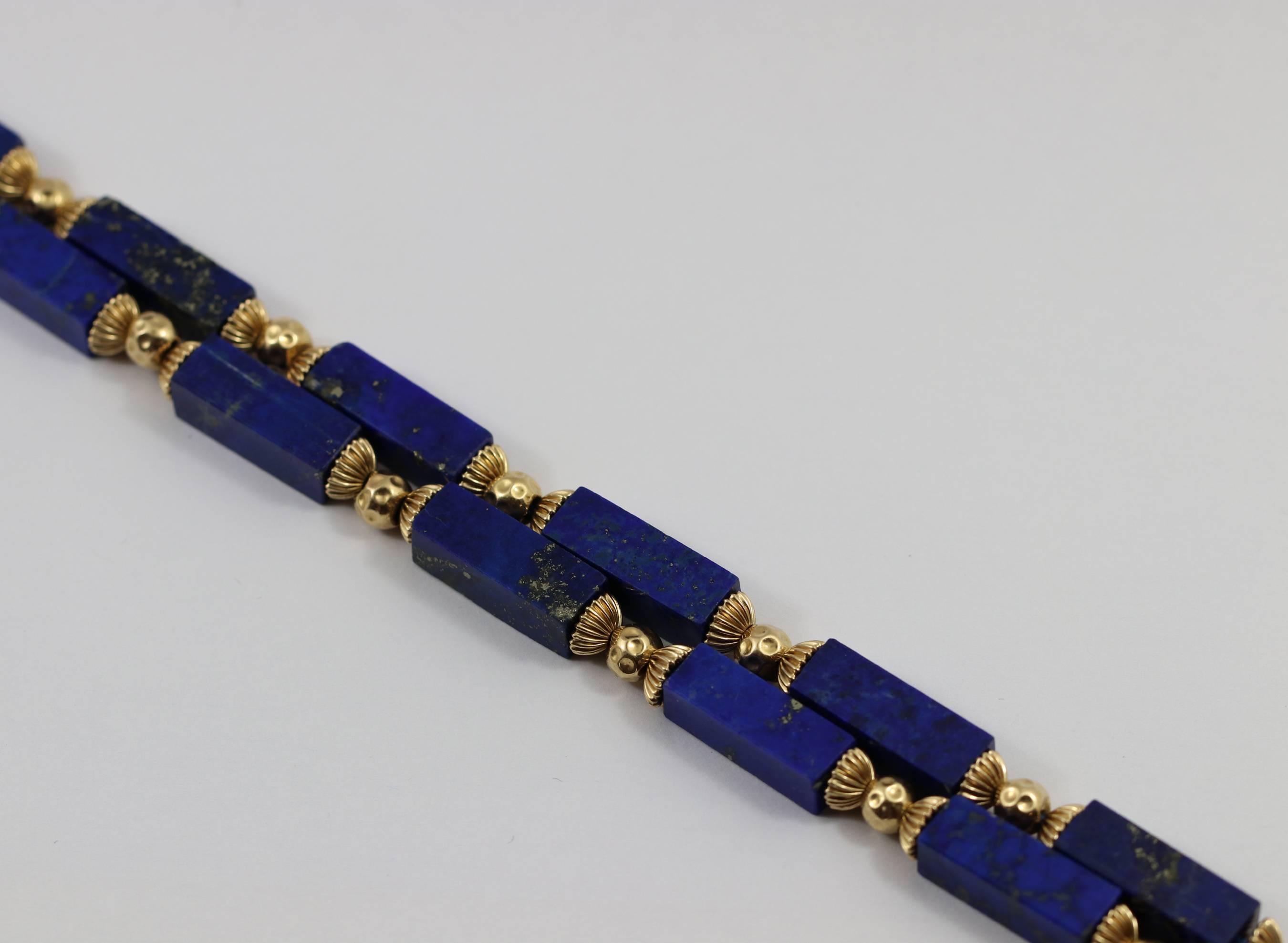 One ladies necklace comprised of 23 rectangular lapis lazuli beads, capped on either end by fluted gold caps, with dimpled gold beads in between. Each piece of lapis measures approximately 20mm X 6mm.