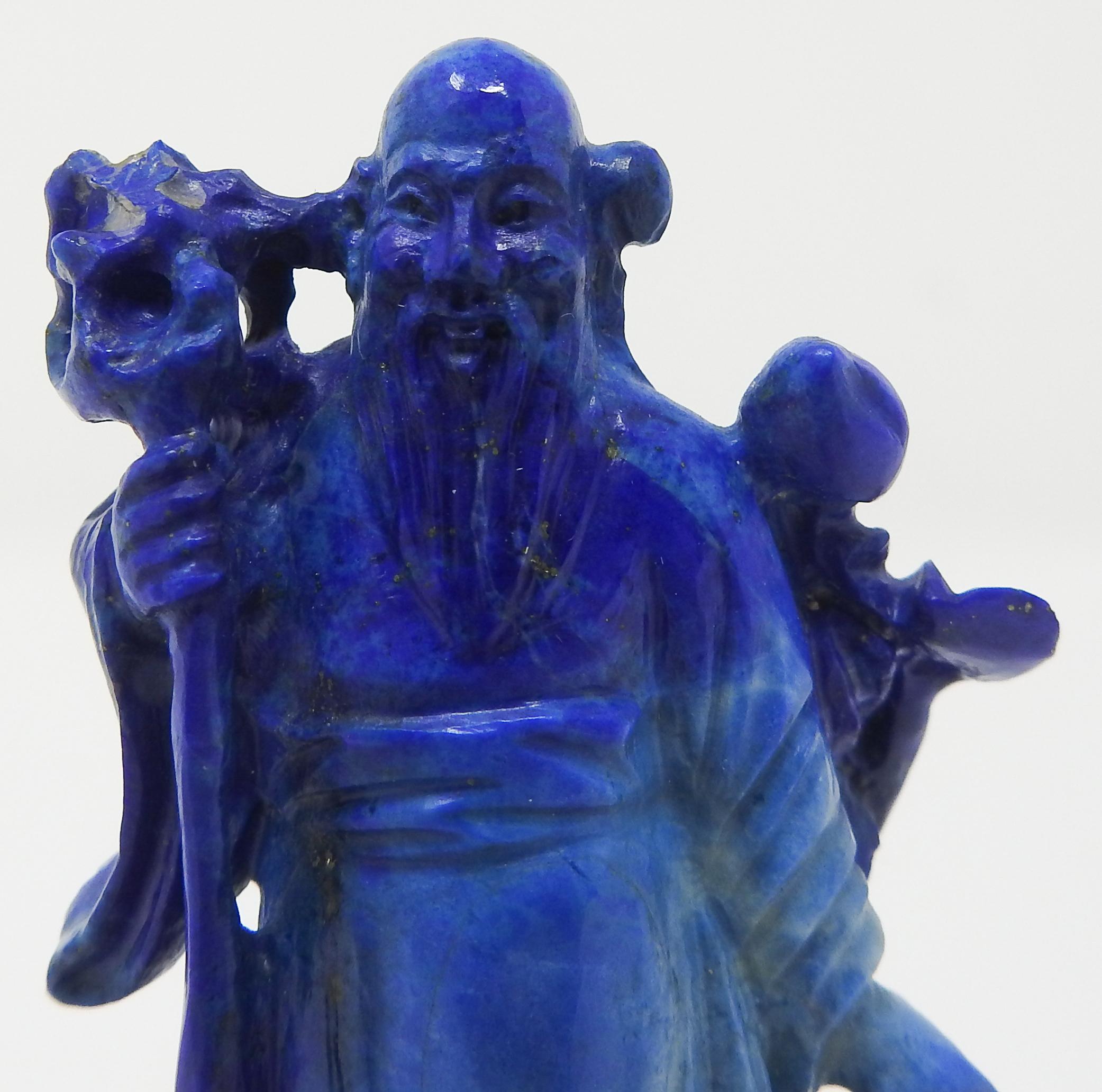 Offering this stunning piece of Lapis Lazuli carved Shou Lao figure from China. He starts on a simple wooden base that has silver inlay. The Shou Lao is gorgeously carved in robes and in one hand has a floral, and the other holding his staff. The
