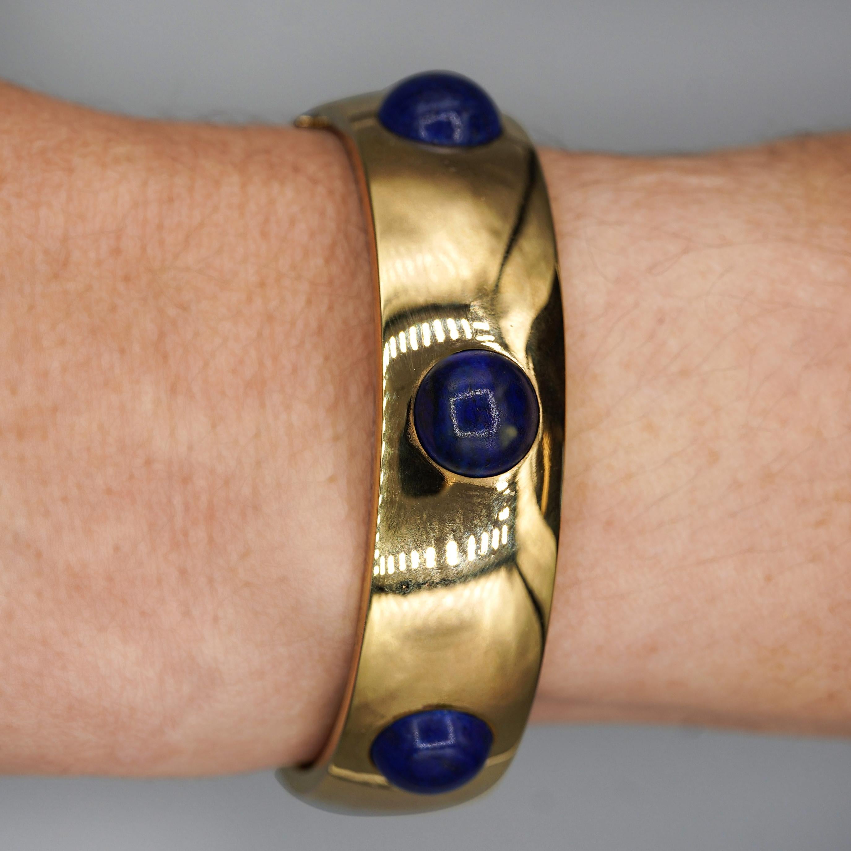 Natürliche Lapislazuli-Cabochons in einem Armreif aus 18 Karat Gelbgold mit 6 bündig gefassten Steinen, einem sicheren Kastenverschluss und einer Sicherheitskette. Armband misst 7 Zoll im Umfang und 16 mm breit.

Einzelheiten:
Artikel Typ: Armspange