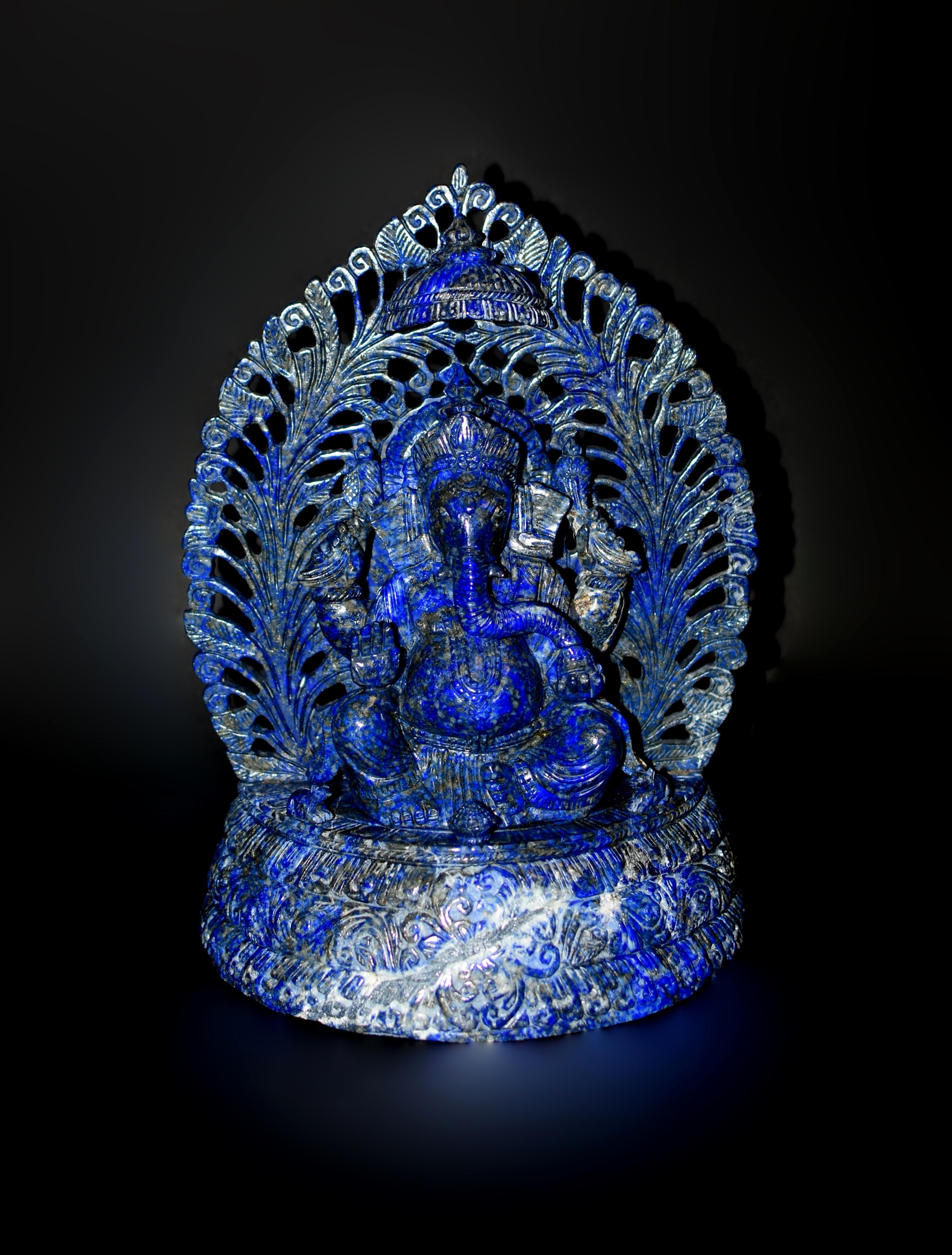 The 9-lb hand-carved natural lapis Ganesh statue is a testament to both artistic brilliance and spiritual symbolism. Adorned in a bejeweled crown, gazing gently with prominent elephantine features, the deity is draped in long necklaces and a cobra