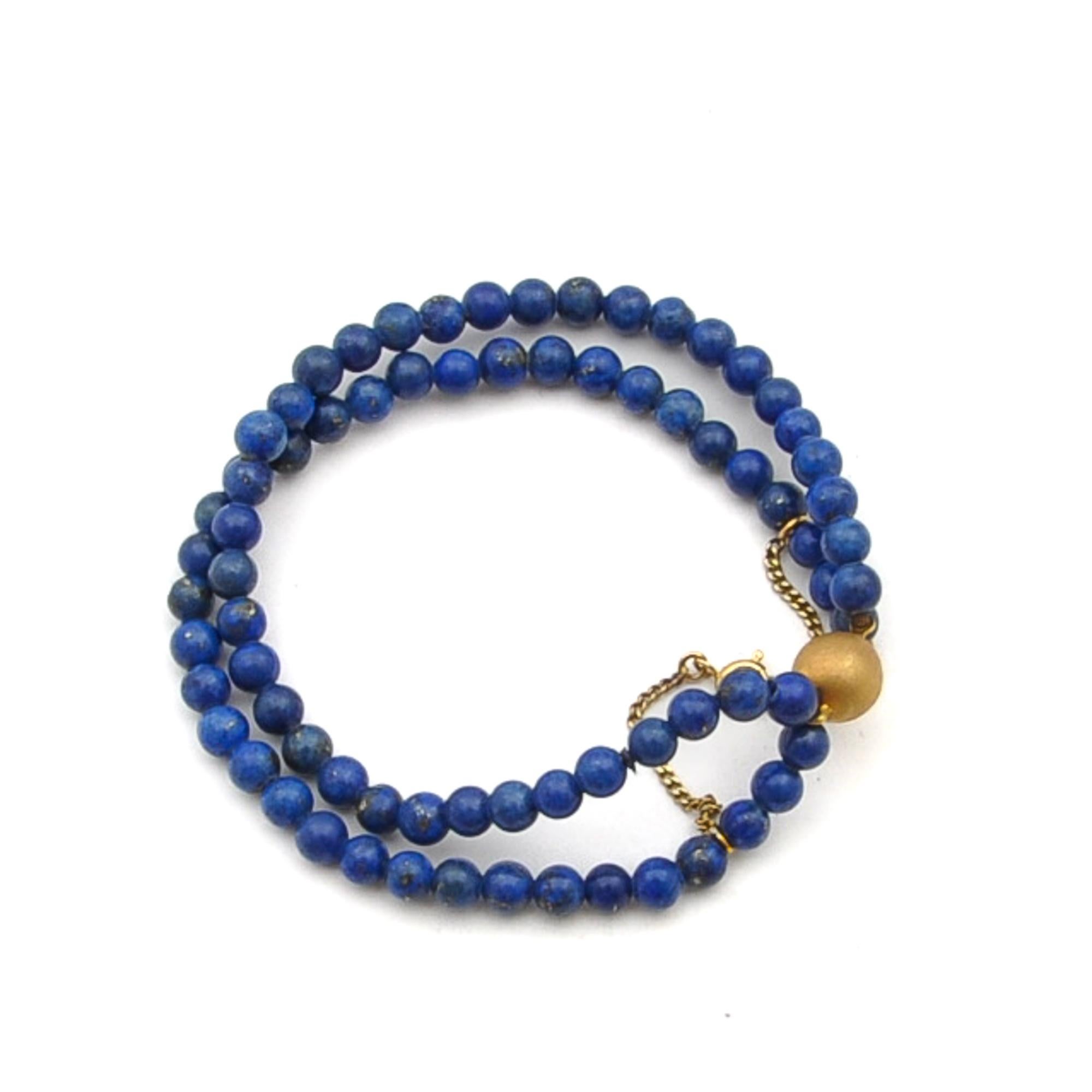 A Mid 20th Century lapis lazuli two-strand beaded bracelet set with a gold ball clasp. The lapis lazuli is smoothly round polished and has a beautiful blue hue and in this royal blue color displaying shimmery spots of gold throughout. Between the