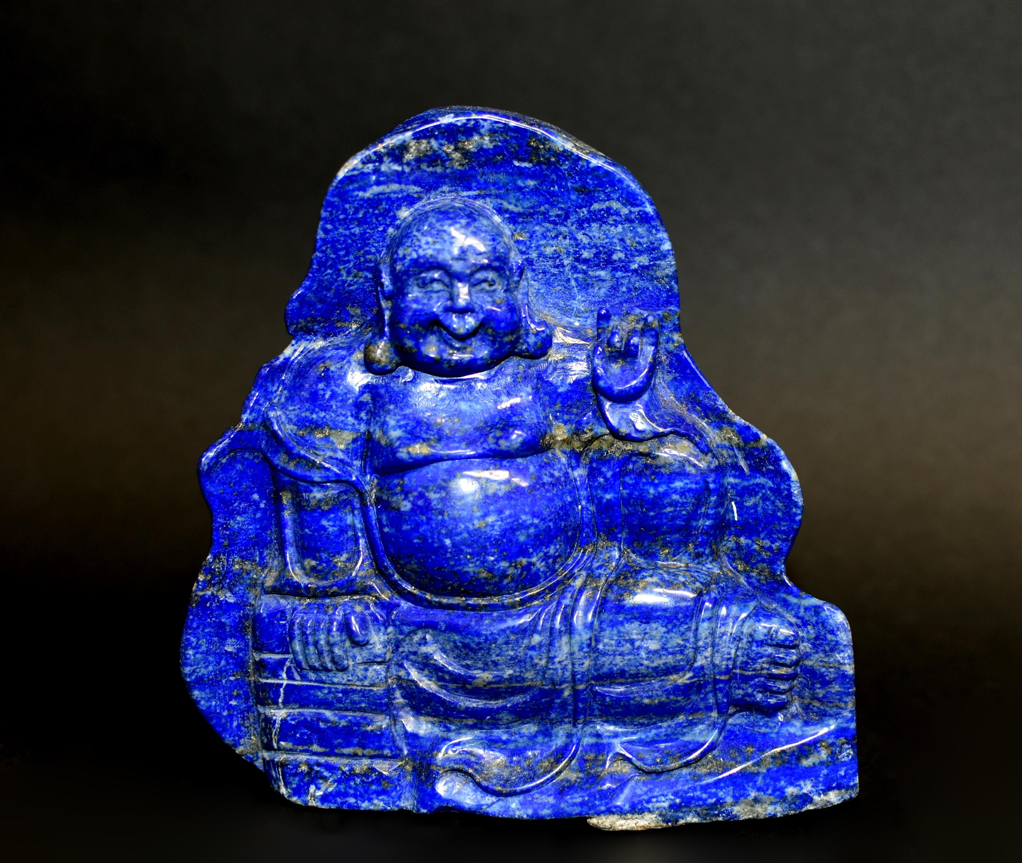 A beautiful natural lapis lazuli statue of the Happy Buddha. The full face with big laughing mouth below smiling eyes flanked by long pendulous earlobes. Buddha wears a loose robe falling gracefully to his legs, revealing his chest and feet. The