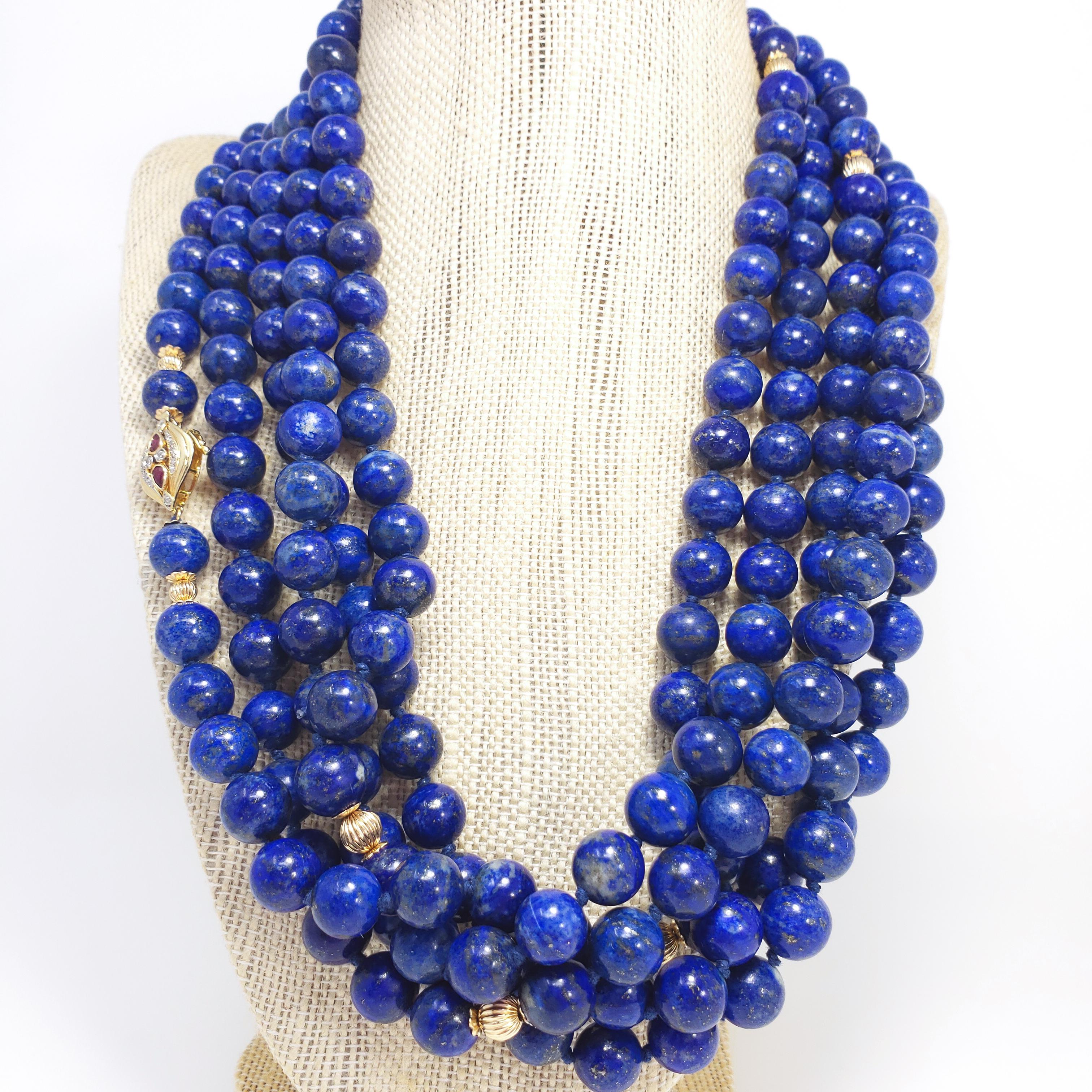 An exquisite, extra long, genuine lapis lazuli bead necklace. Features a single strand of 10mm lapis lazuli beads accented with 14K gold accents and spacers. The 14 karat gold clasp is decorated with two pear-shaped rubies (0.39 total carats) and 14