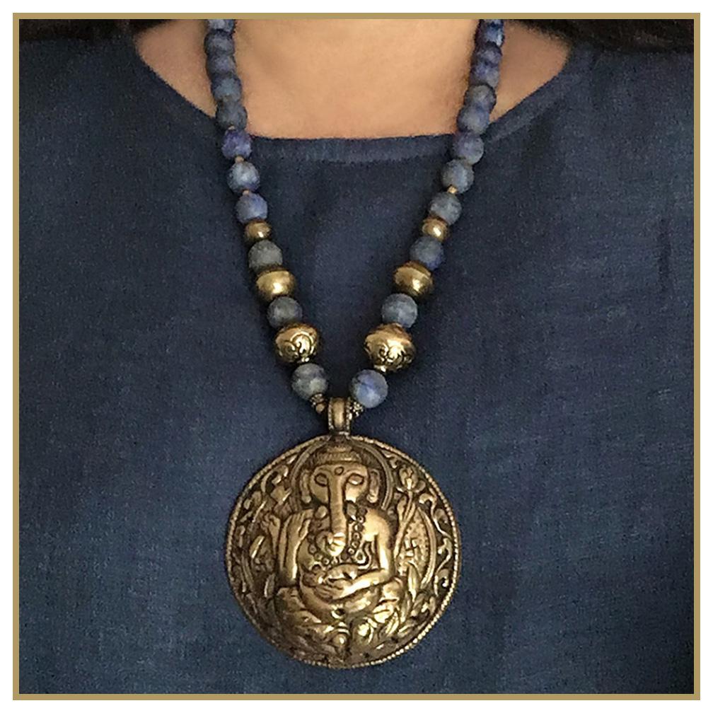 This is a Lapis Lazuli necklace with Ganesha* pendant. Nouveau Boutique created this long strand necklace with 12 mm matte finish Lapis Lazuli beads, vintage brass spacers, gilt toggle clasp and a Nepal handcrafted 3 inch diameter brass Ganesha