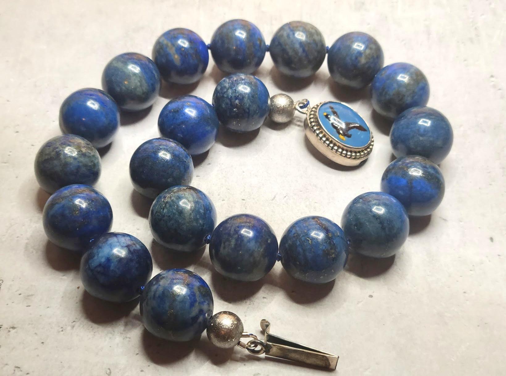 This necklace measures 18 inches (45.7 cm) in length and features smooth, round beads, each 20 mm in size. The lapis lazuli beads showcase a deep indigo, midnight tone with natural calcite and golden pyrite flecks. These beads are entirely natural