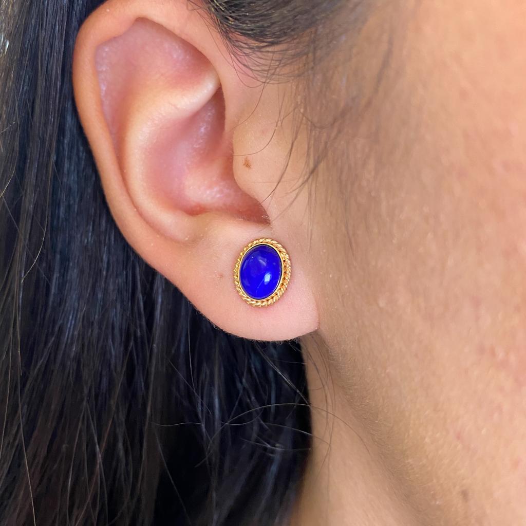 These lovely lapis lazuli stud earrings give a graceful pop of color to your ears. The frame of the earrings are made in 14 karat yellow gold. The lapis lazuli oval cabochons sit in a lovely collar of gold with a 1 millimeter (mm) twisted wire