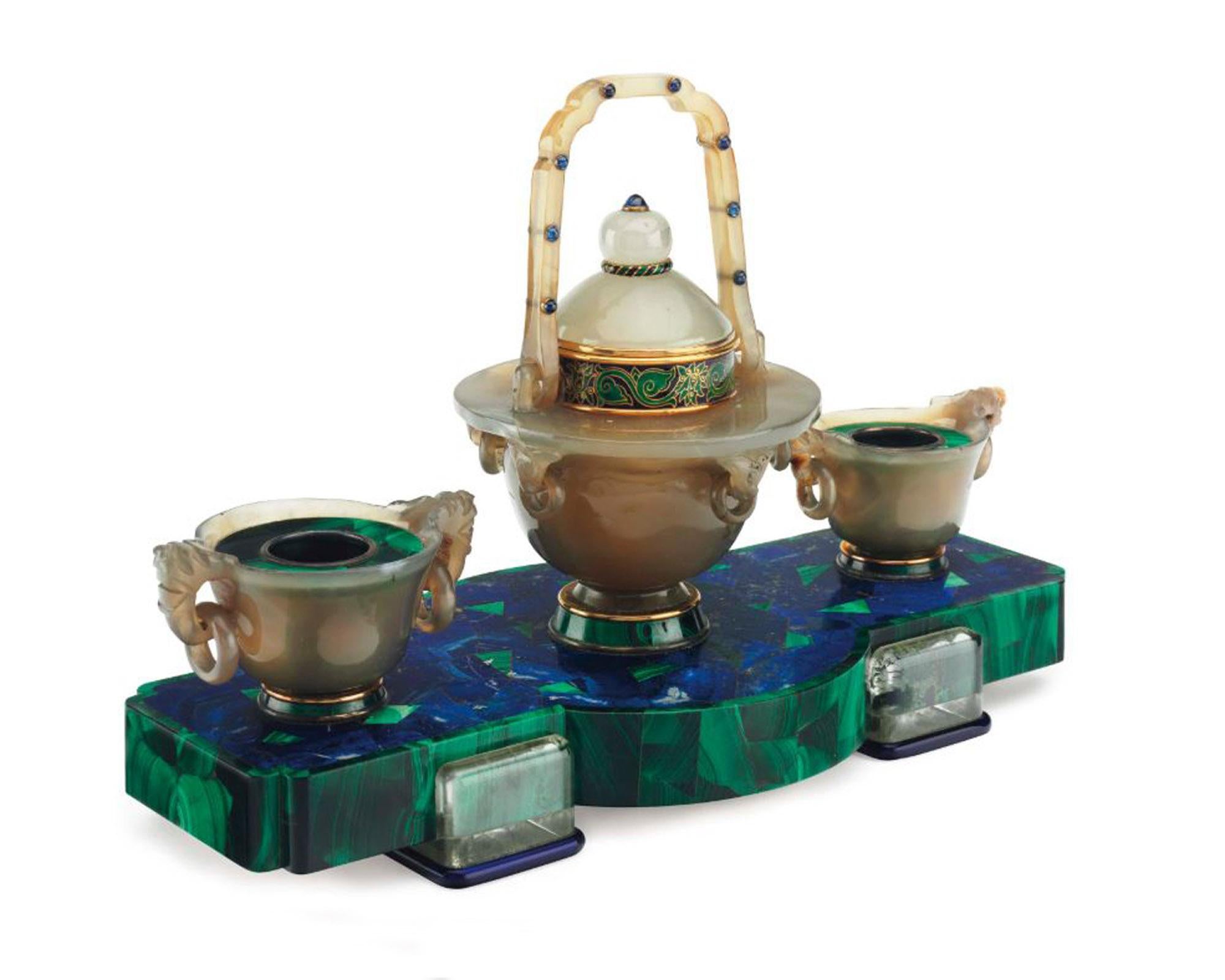 Un extraordinario tintero Art Déco de Cartier.  
Base rectangular de malaquita y lapislázuli con motivo de mosaico,
sostenida por pies de cristal de roca y esmalte azul, engastada en el centro con un ágata y 
tintero de zafiro cabujón, realzado con