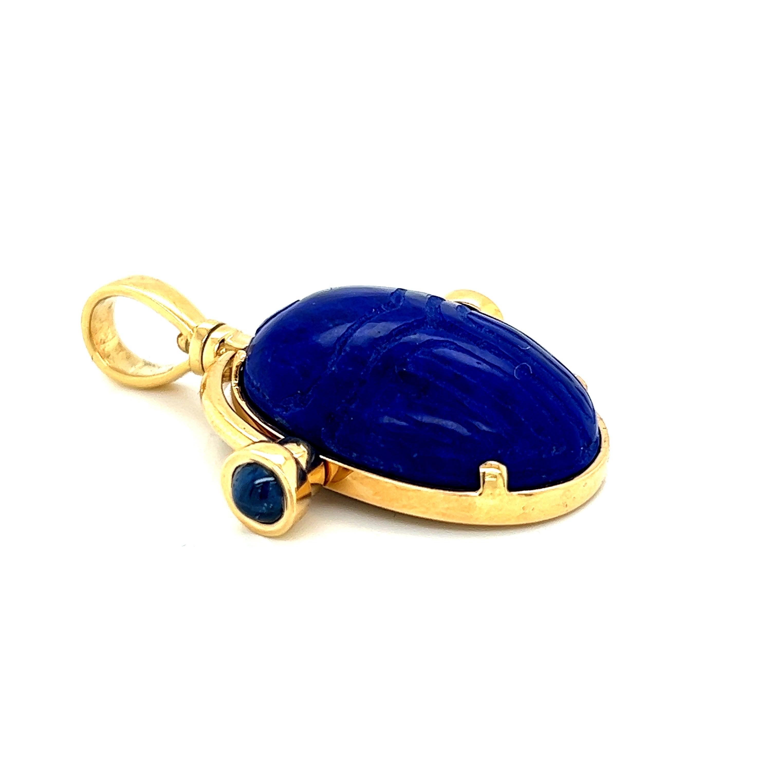 Hand carved scarab Lapis Lazuli pendant in 18k yellow gold with cabochon sapphires.
The scarab was carved by an artist in the United States and his signature is featured on the back of the scarab.

The pendant measurements are: H (including bail):