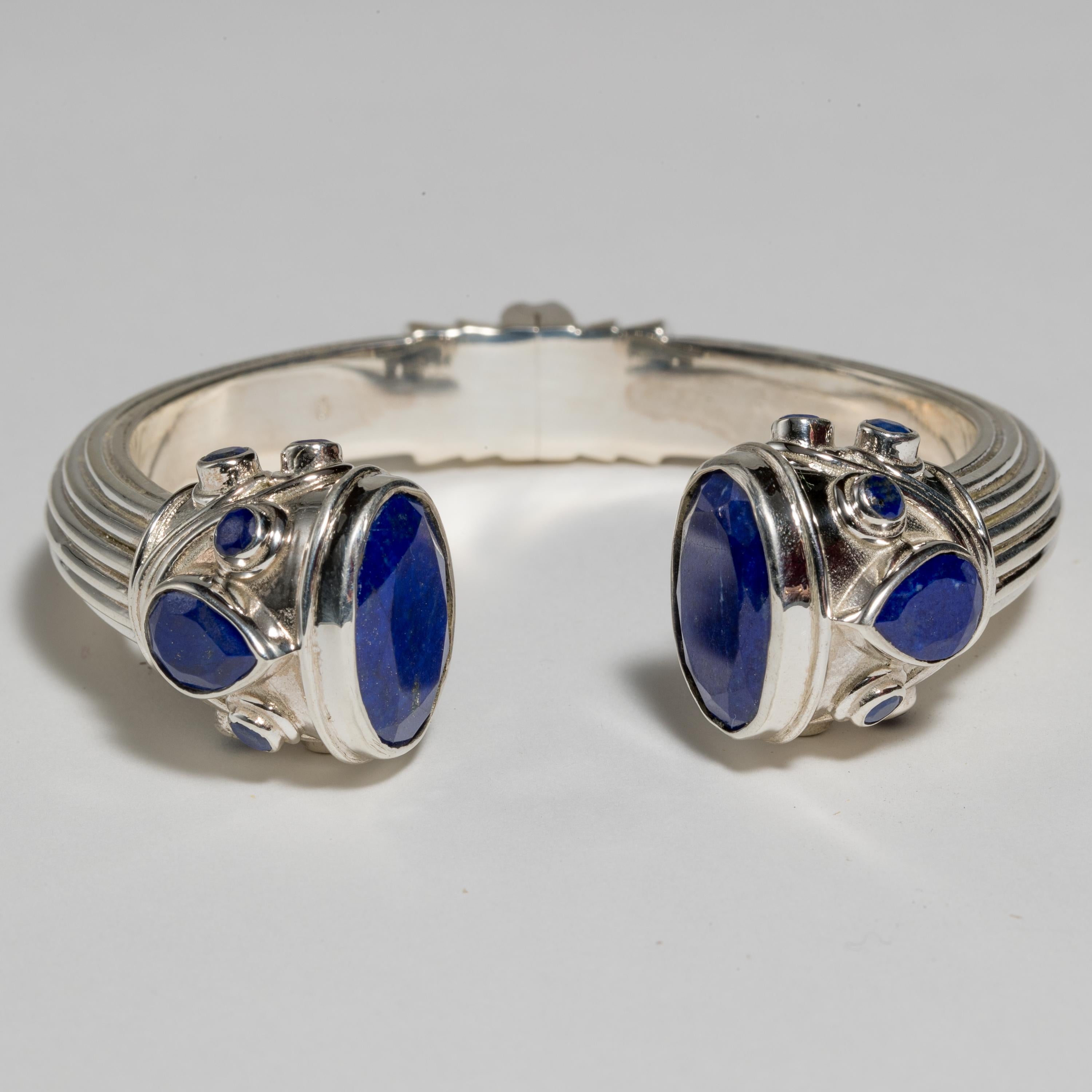 A hinged cuff clamper bracelet with textured sterling silver sides and faceted lapis lazuli pear-shaped and round stones on top of the bracelet and large faceted oval lapis on top inside. Natural lapis with beautiful peacock blue color.  The inside