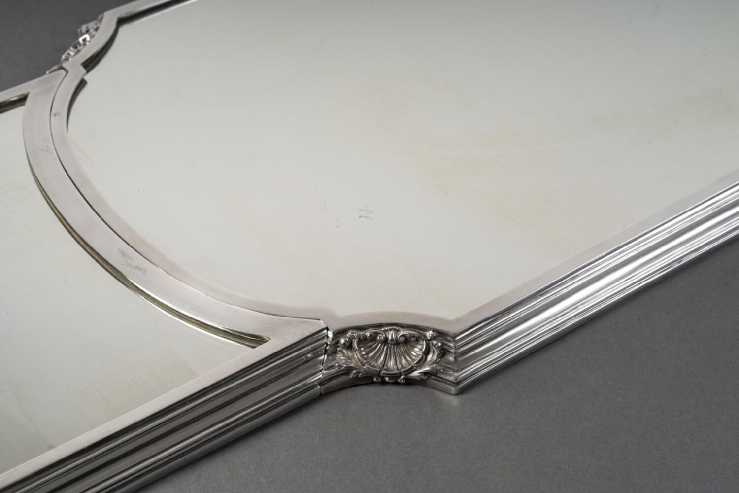Three-part mirror-based table centrepiece, mounted on an oak parquet floor, surrounded by a large silver-plated bronze ingot mold, decorated with shells in the curved parts; the two sides fitting separately on the center;

Dimensions: length 143 -