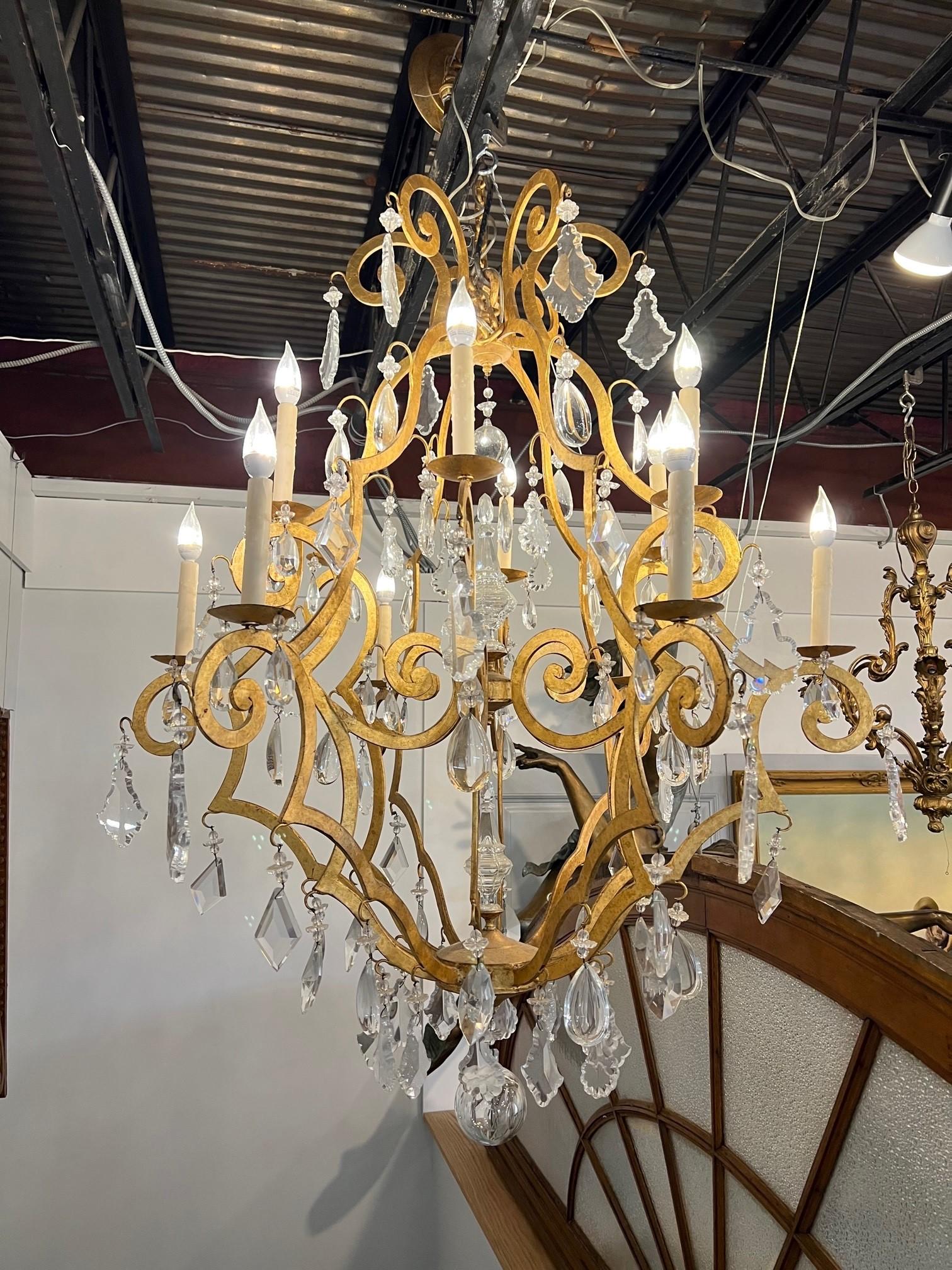 Large iron and crystal chandelier, gold finish and 12 lights. It has six different size and shape crystals hang from the chandelier which gives it a good look. The lights are candelabra size and all are in working condition. Salvaged from a home in