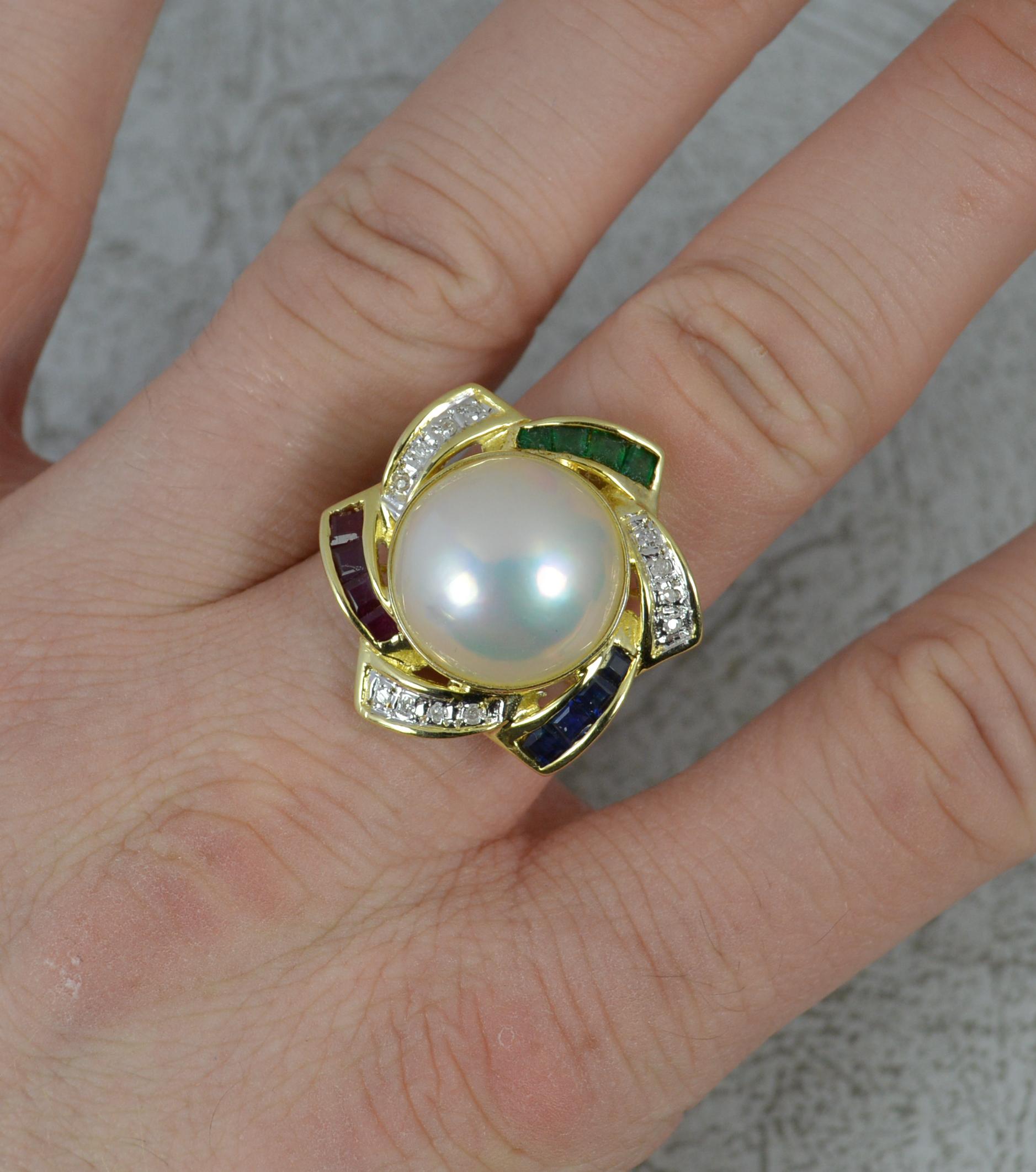 A superb Pearl, gemstone and diamond cluster ring.
Solid 14 carat yellow gold example.
Designed with a large Mabe Pearl to the centre, 15mm diameter. Surrounding are alternating sections of round brilliant cut diamonds and princess cut ruby, emerald