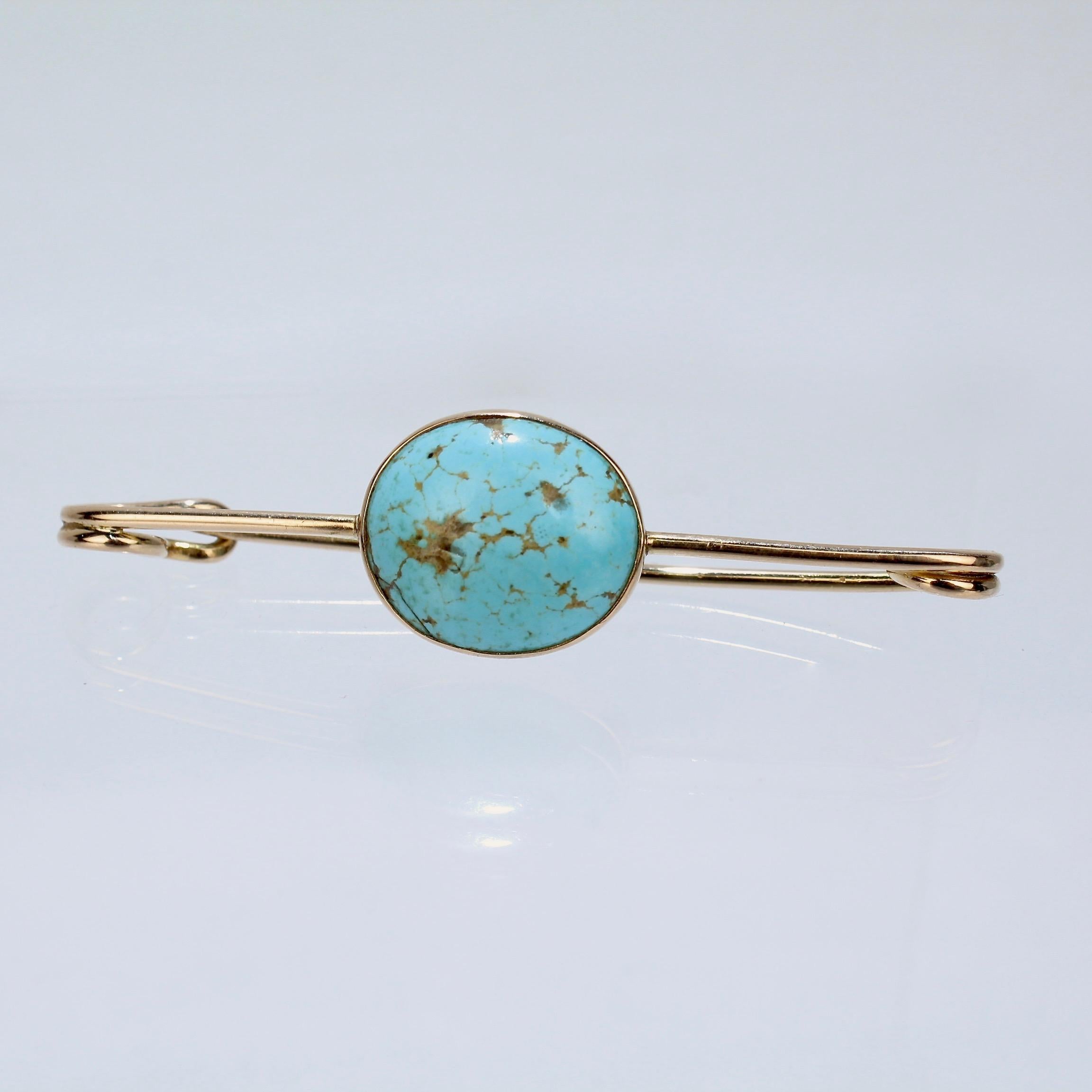 A very fine 14k gold and turquoise scarf pin or brooch.

Fashioned as a bar pin and bezel set with a beautiful turquoise matrix cabochon to the center.

The reverse having a coiled spring and straight pin that is secured in a safety-pin