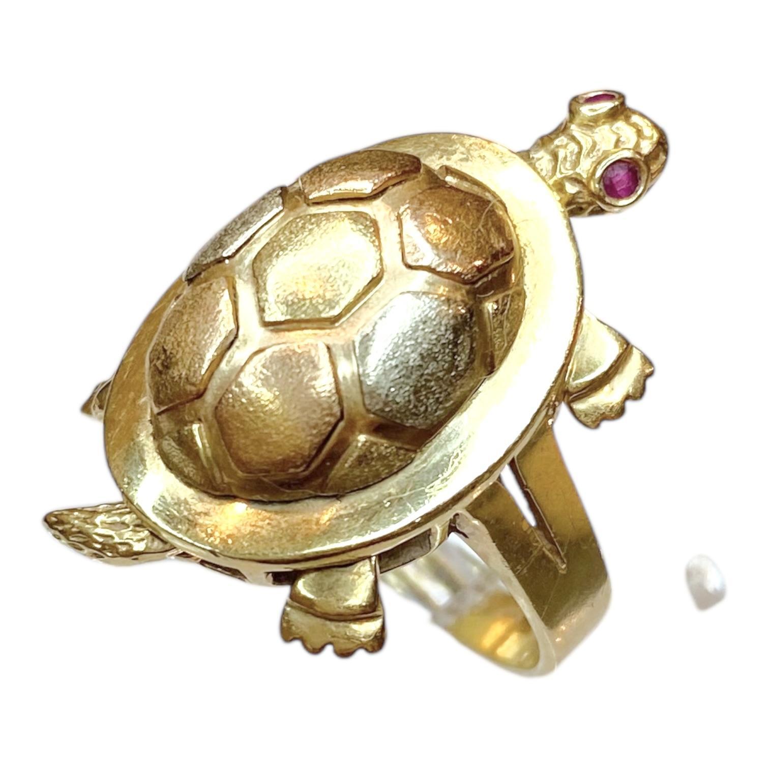 Realizzato in oro giallo 14 carati, l'anello presenta un motivo di tartaruga articolata (testa, gambe e coda si muovono). Gli occhi della tartaruga sono incastonati con rubini di taglio rotondo e il guscio è intricato con un motivo esagonale in oro